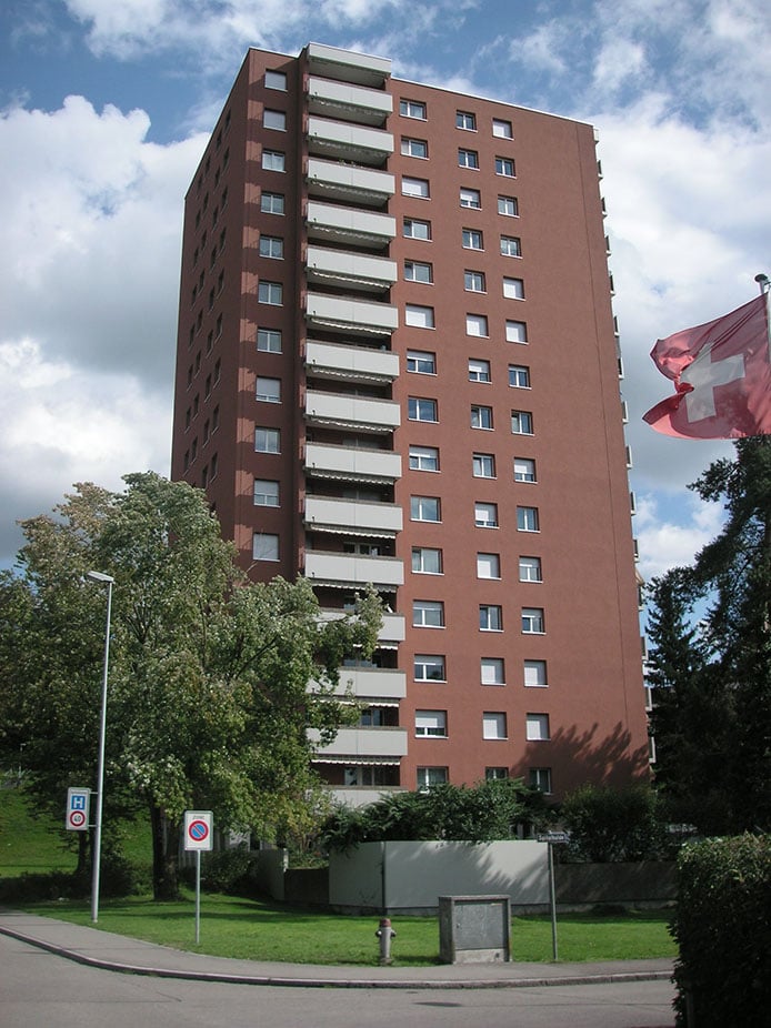 high-rise brown brick apartment building, many windows, balconies, street sign, Swiss flag