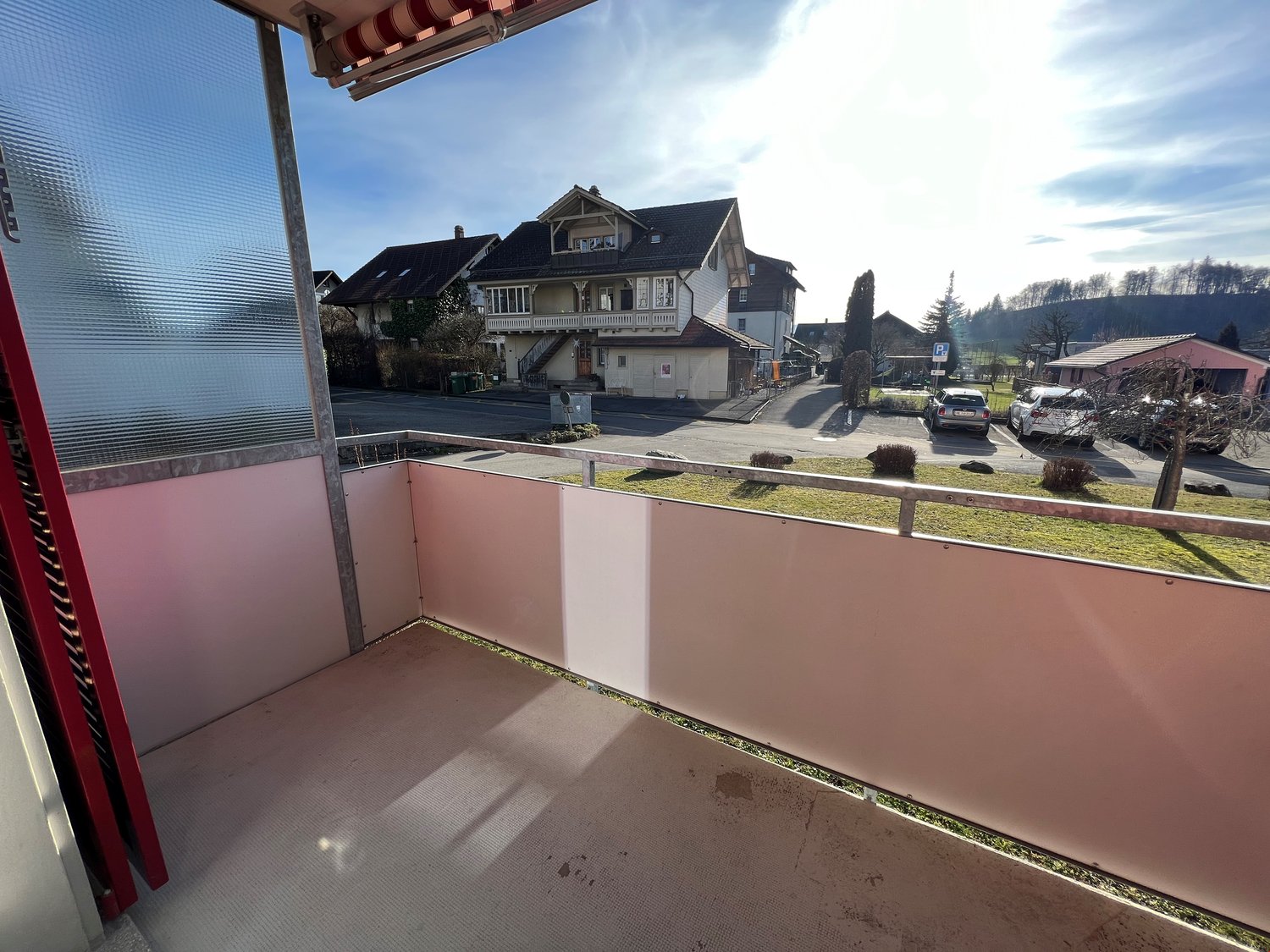 View of the town from the balcony, large glass window, balcony railings, grass and parked cars