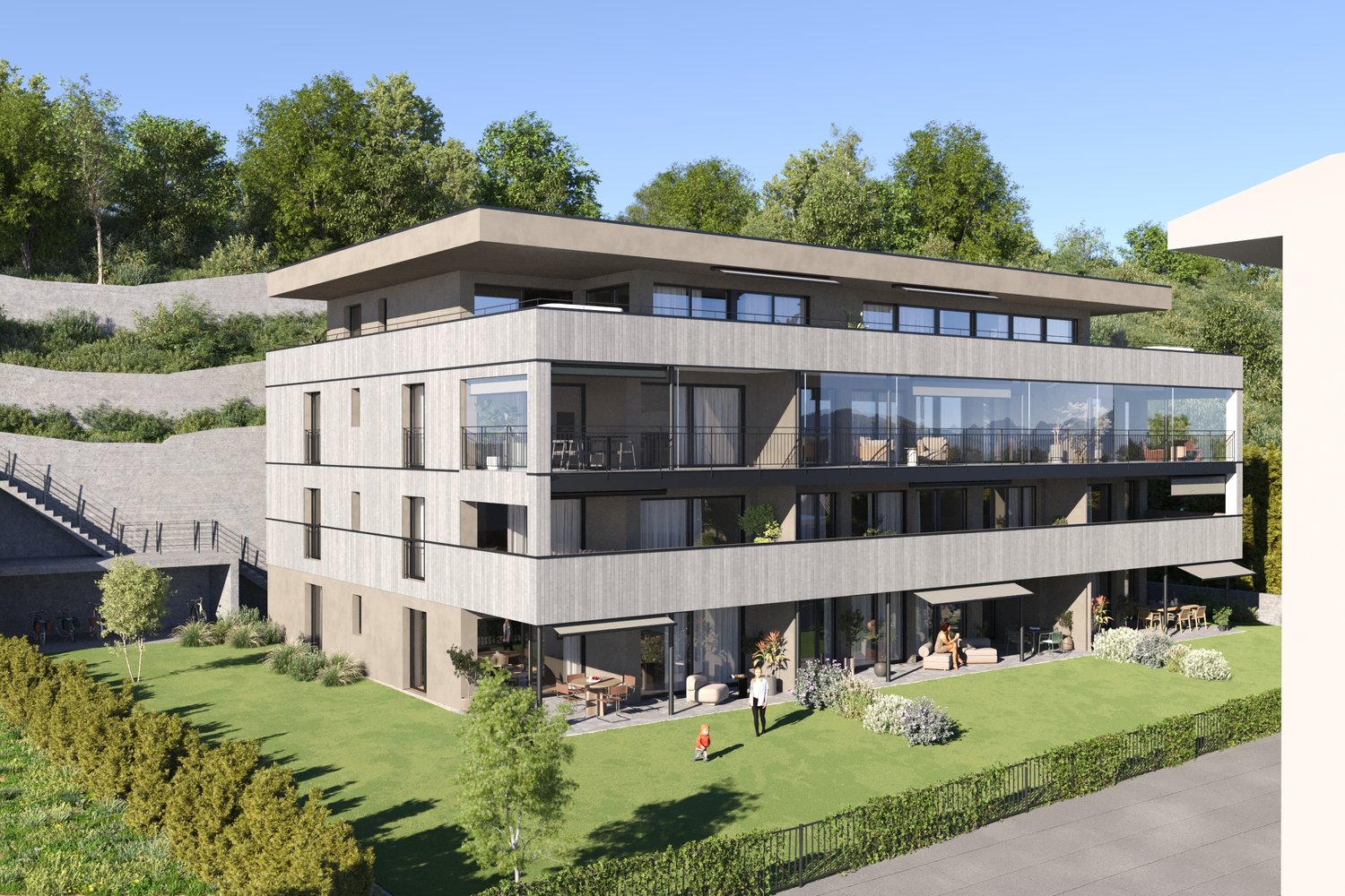 3-story modern apartment building with a flat roof, large windows, and balconies. The building is surrounded by lush greenery and landscaping, including a grassy area in the foreground. There appears to be a parking area or driveway adjacent to the buildi