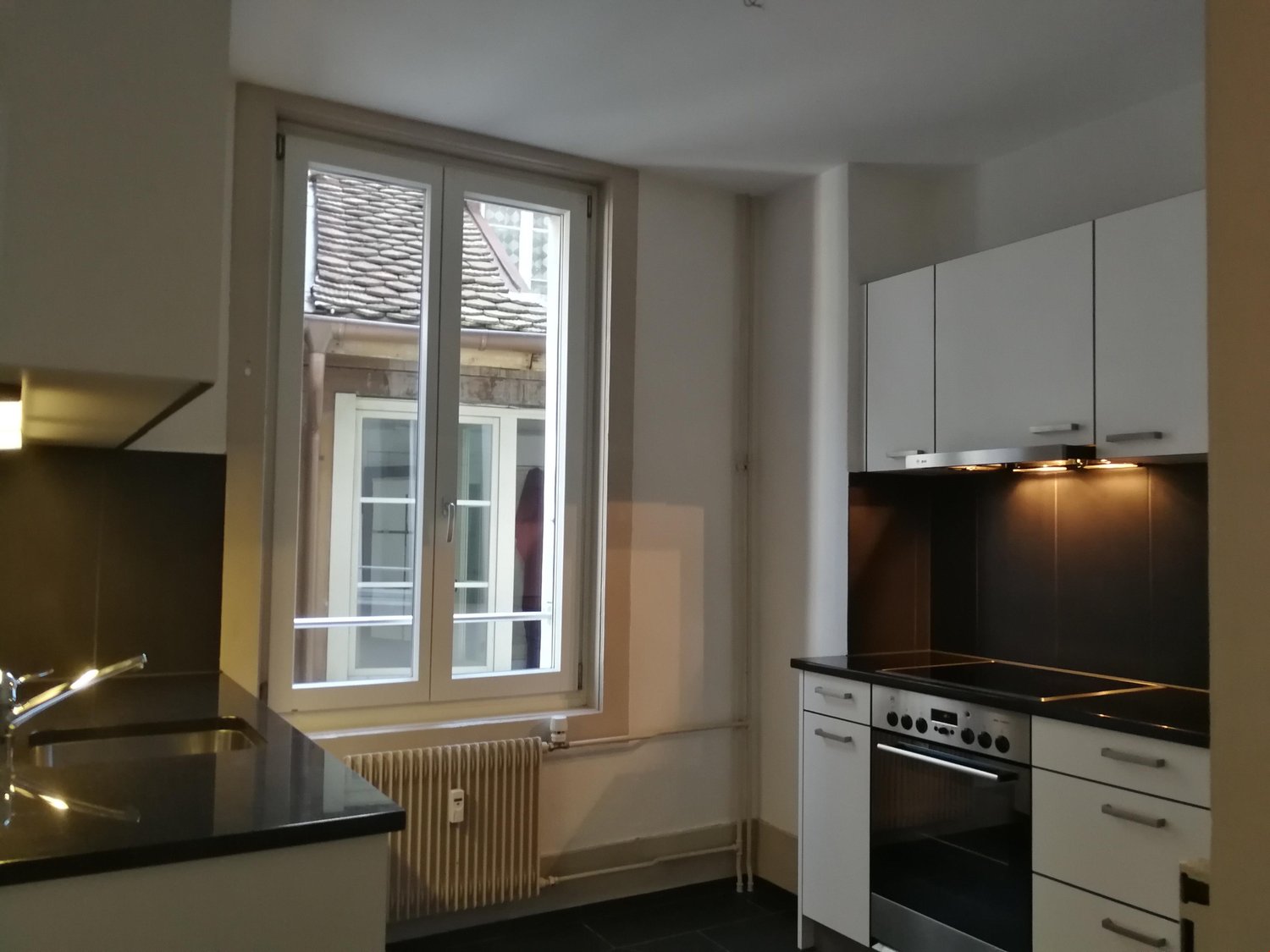 Modern kitchen with window, white cabinets, black countertop, sink, stove, oven, kitchen appliances, window with view, heating radiator