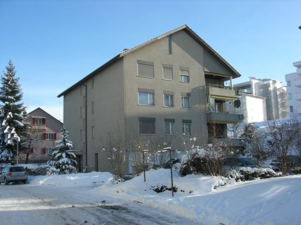 Apartment building, raised ground floor, multiple windows, covered parking, snow, nearby tree, cars parked
