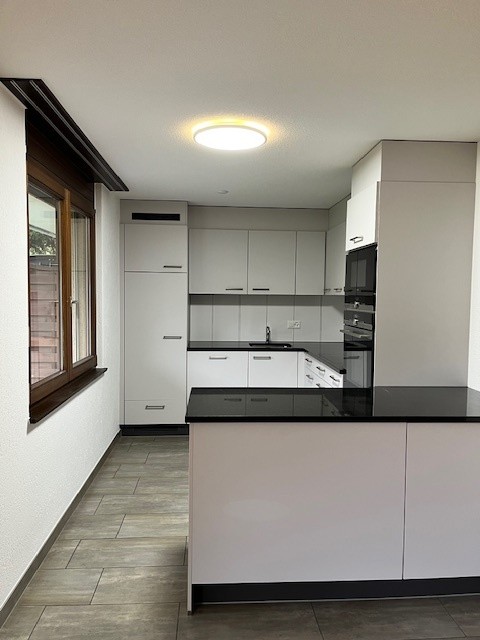 White kitchen cabinets, black counter top, white sink, under-cabinet lighting, microwave, stove, modern design