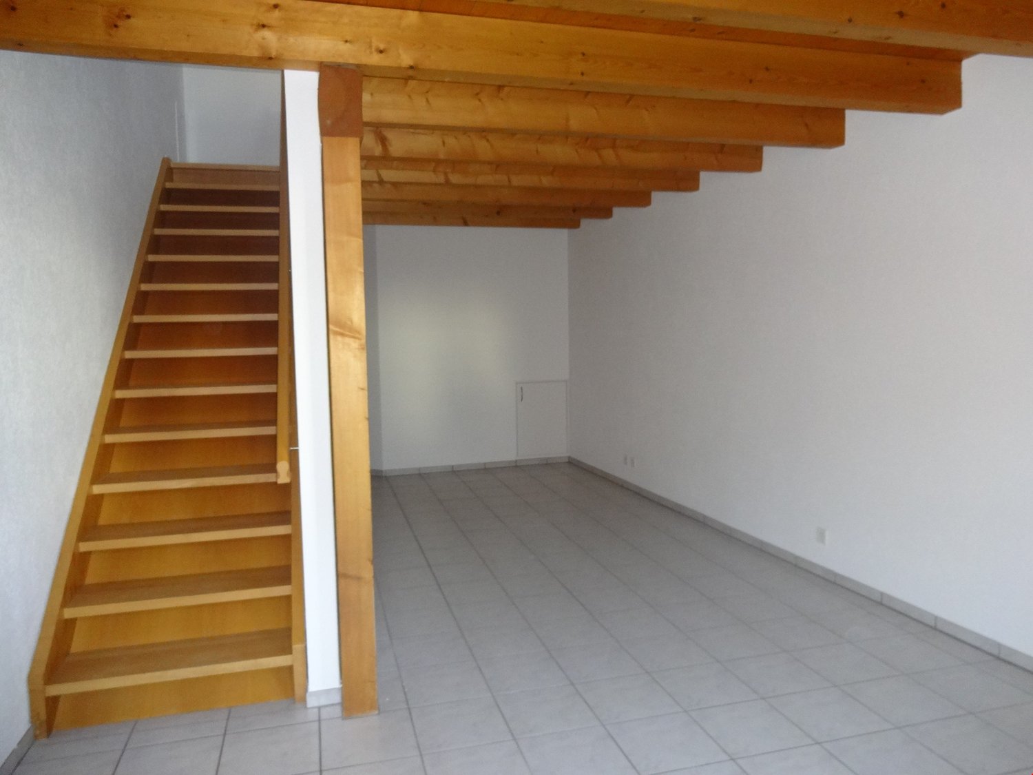 empty room with white walls, wooden ceiling beams, and tiled floor, a staircase on the left side