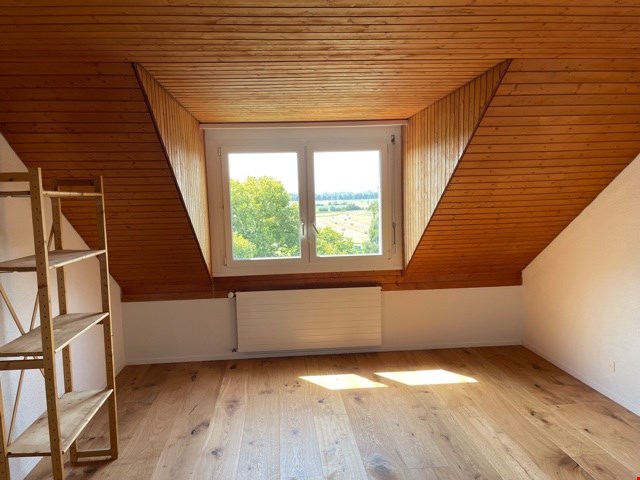 empty attic room with wooden beams, window, hardwood floor, and a shelf