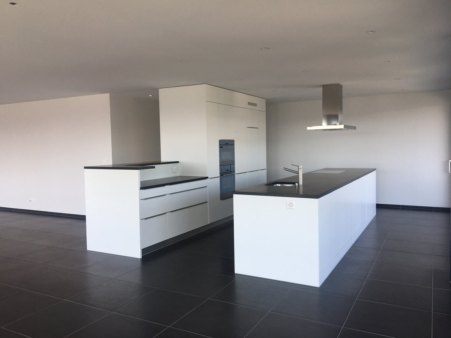 modern kitchen with white cupboards, black tiles, island with sink and faucet, stove and oven