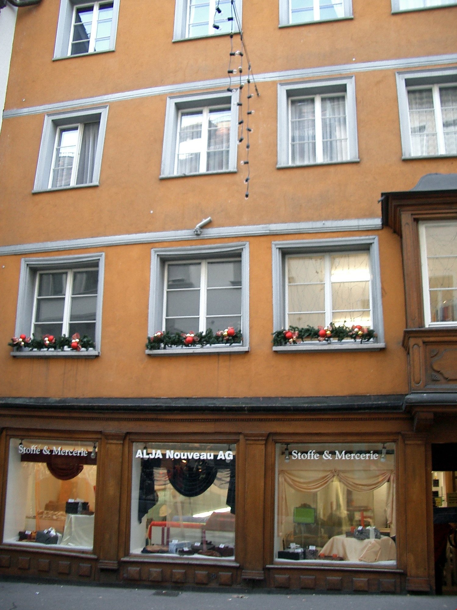 orange building, windows with white frames, holiday decorations on the windows, storefronts with window displays