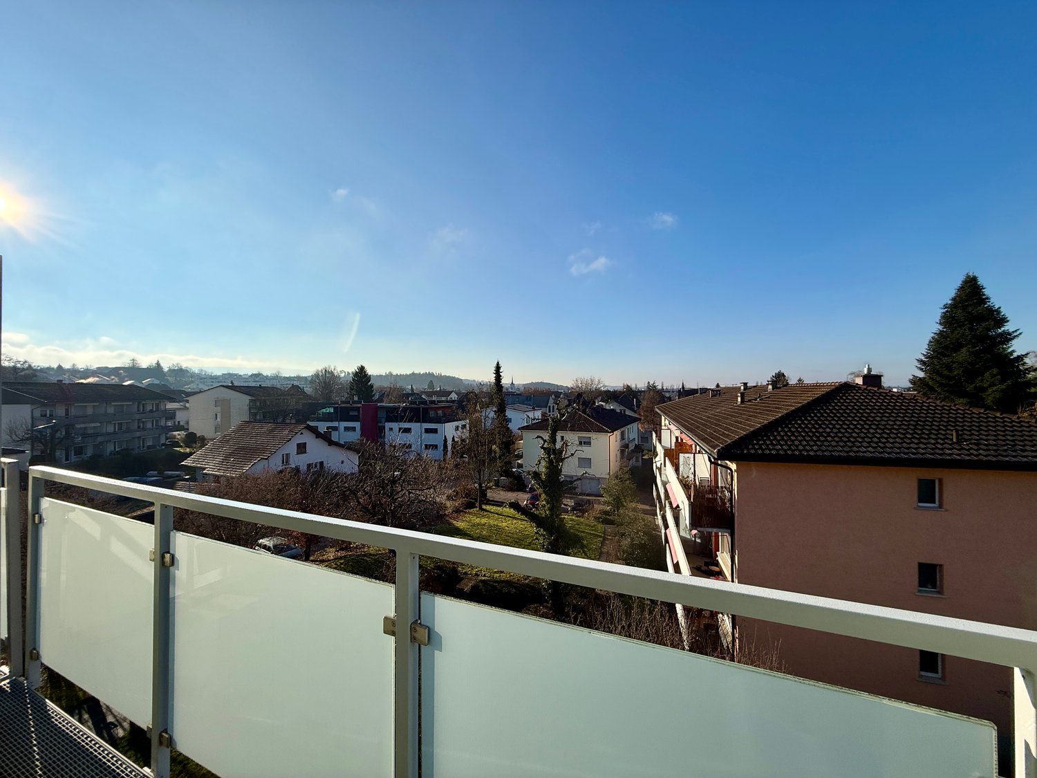 Balcony with a panoramic view, surrounded by other buildings, clear sky, and trees.
