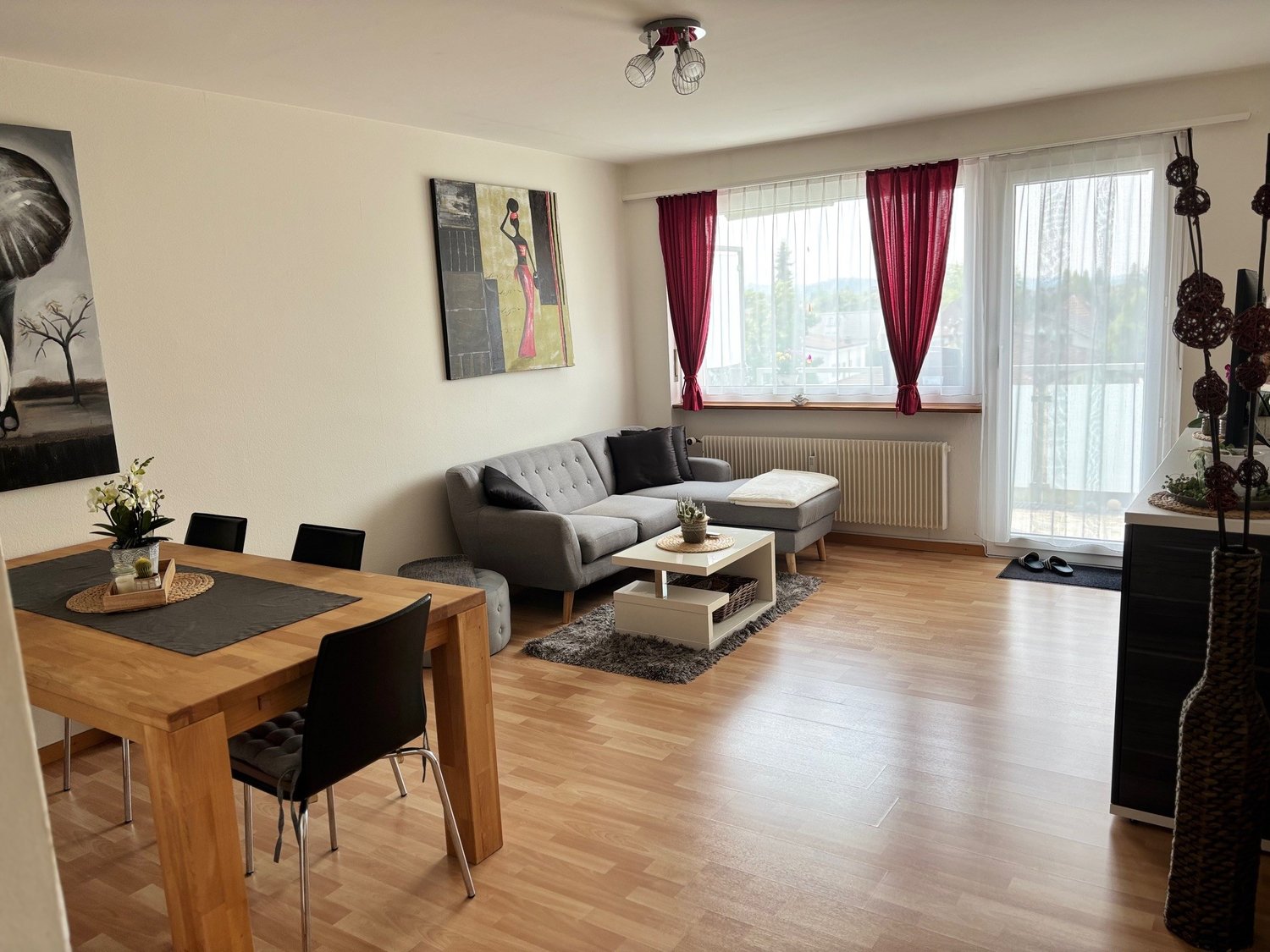 Wooden floor, grey couch, white coffee table, dining table, four chairs, picture, radiator
