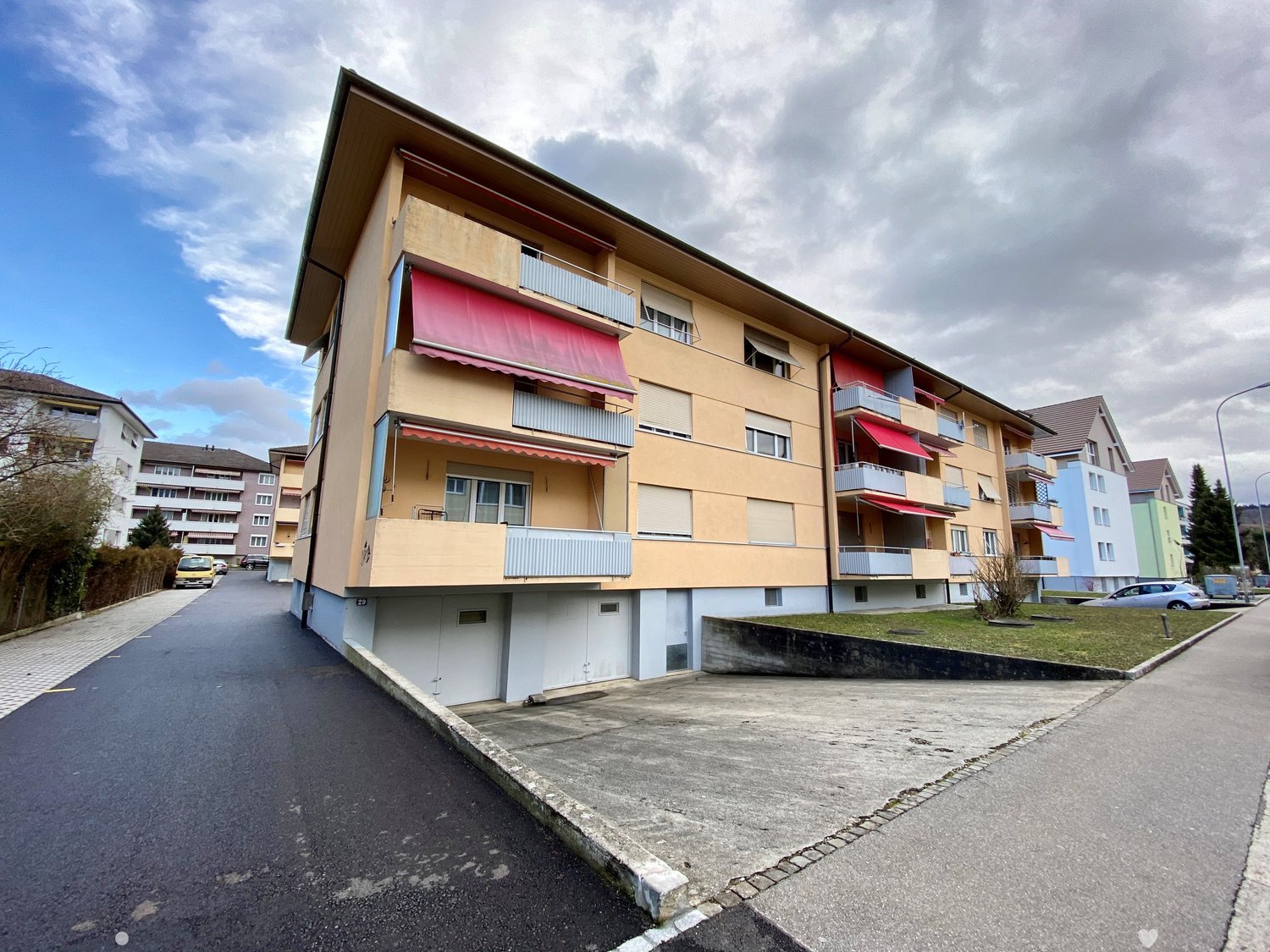 3 story apartment building, beige walls, red roofs, multiple balconies, parking lot, side walk