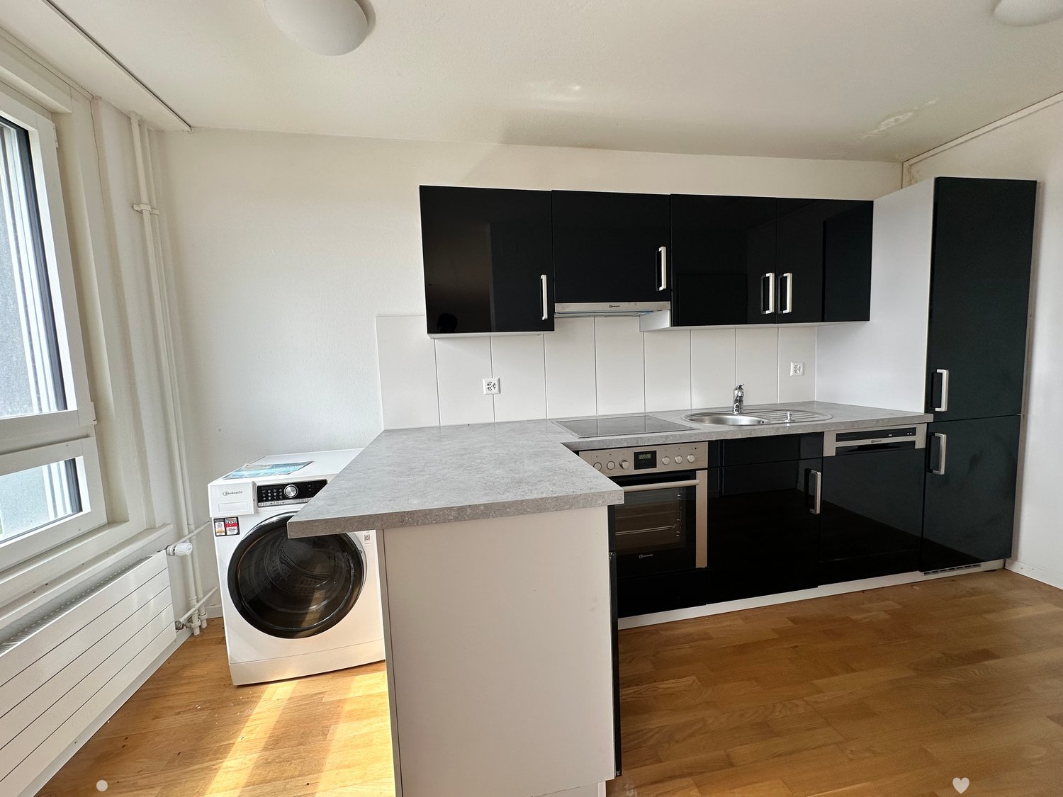 Kitchen with a washing machine and dishwasher, black cabinets, a grey countertop, wooden floor, a gas stove, a sink, and a window.