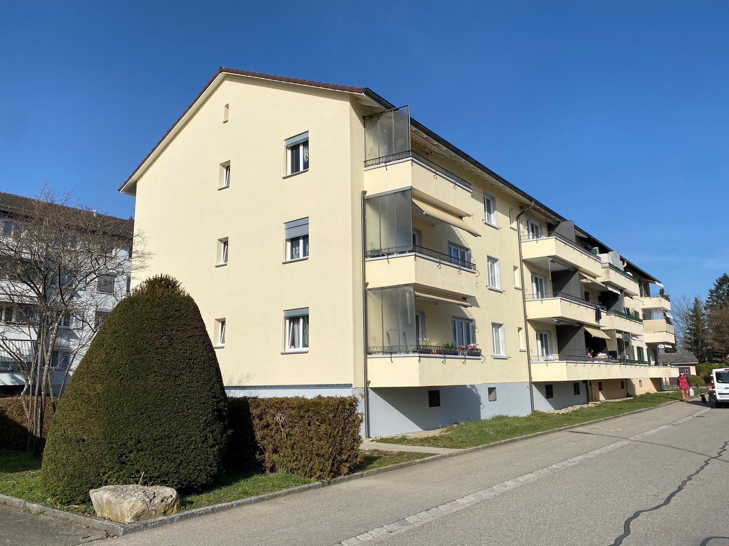 3-story building, yellow exterior, multiple balconies, green shrubbery