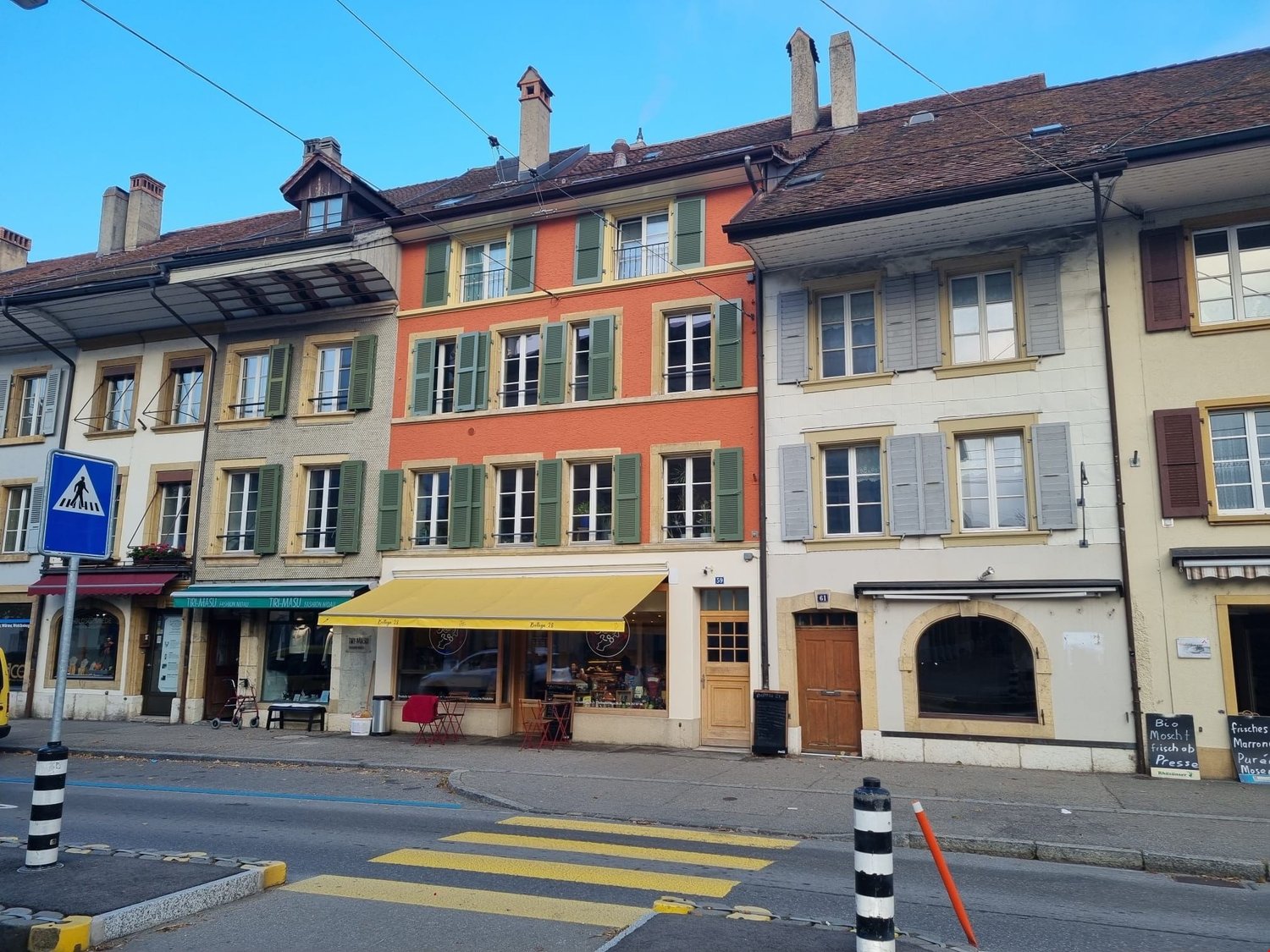 Three story commercial buildings with shops and a yellow awning at the center. Multiple windows, satellite dishes, trash bins outside.
