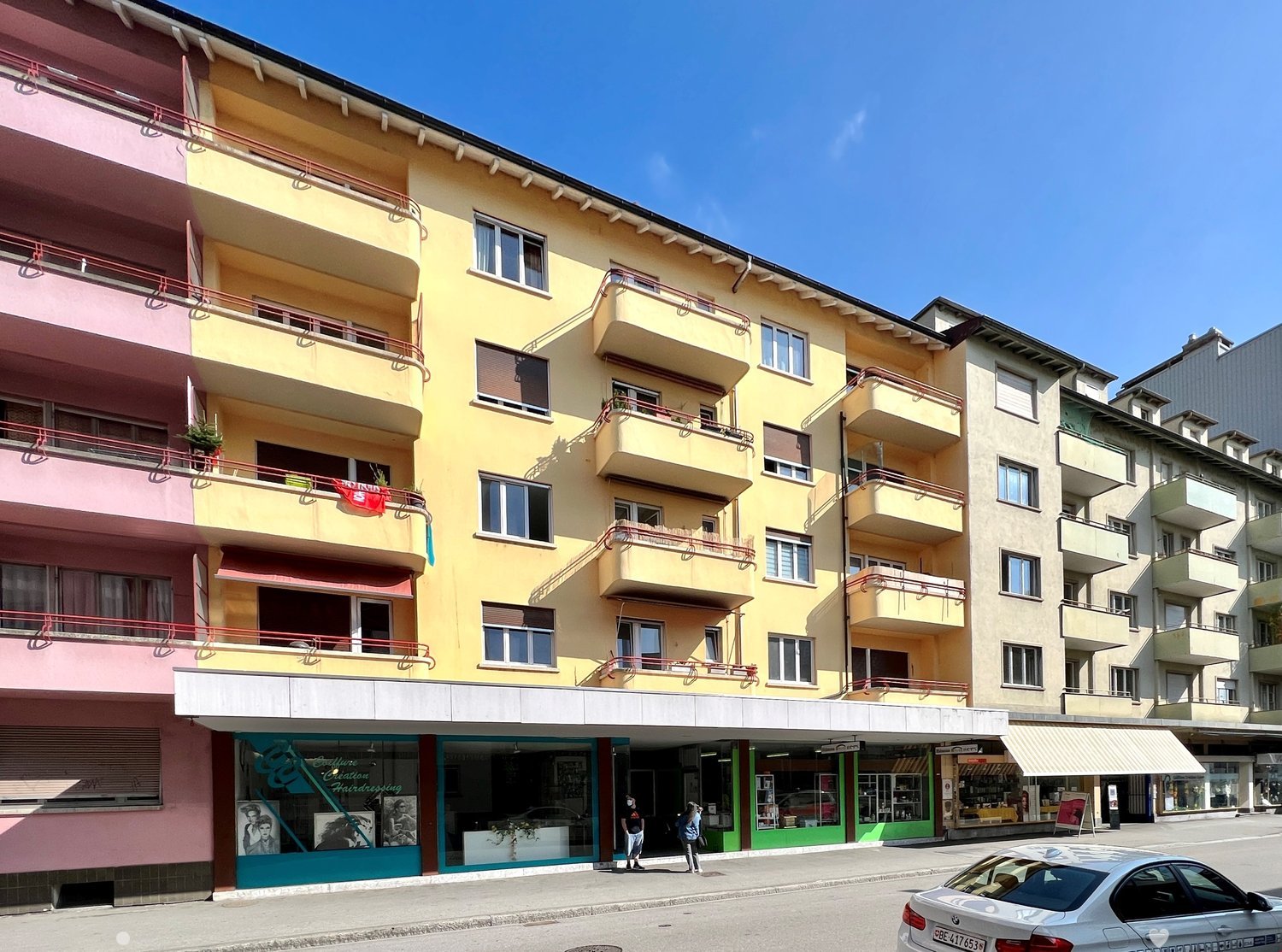yellow 5 story building with multiple balconies and windows, stores on the ground floor