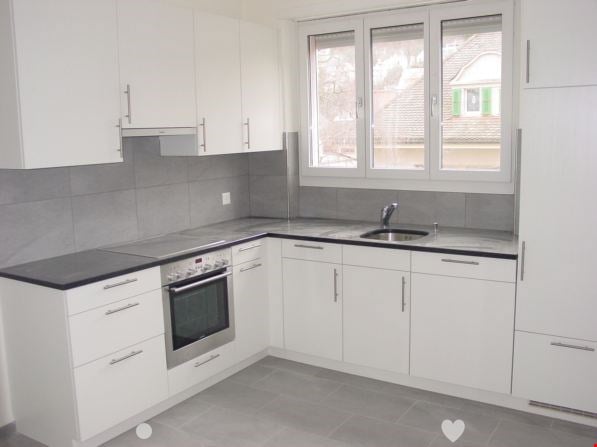 Modern, L-shaped kitchen with white cabinets, black countertops, and stainless steel appliances including a dishwasher. Large windows provide natural light.