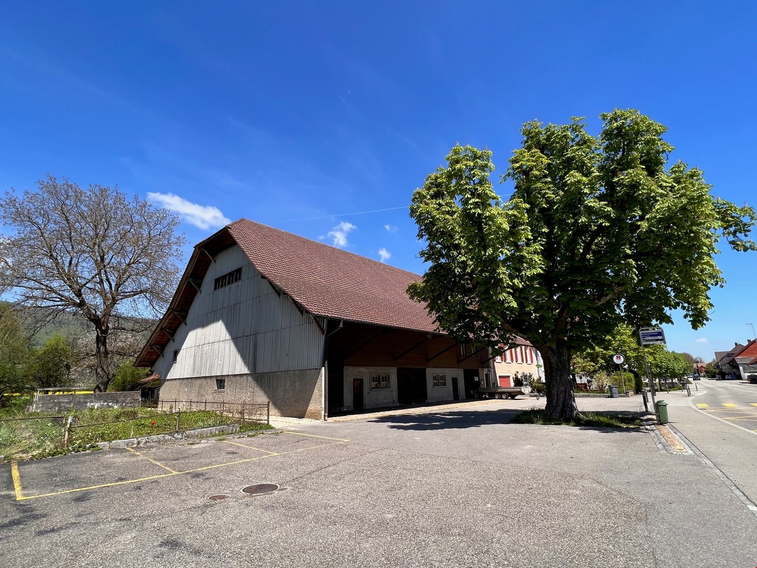 Warehouse with brown roof, concrete base, parking lot in front, trees on both sides