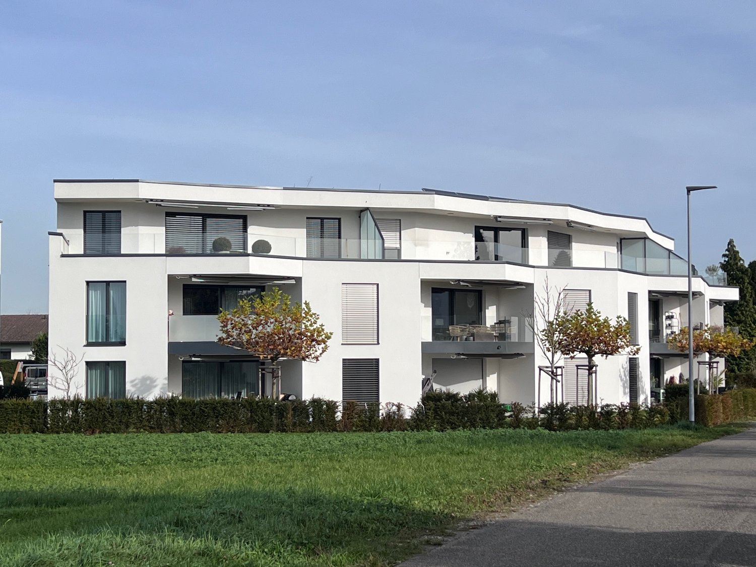 modern apartment building, white, glass windows, balconies, solar panels on the roof
