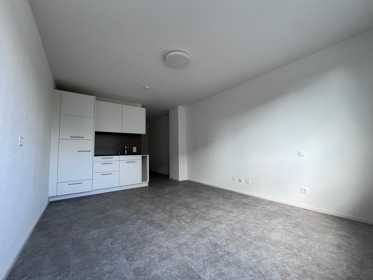 empty room with gray floors, white walls, built-in cabinets, and electrical outlets