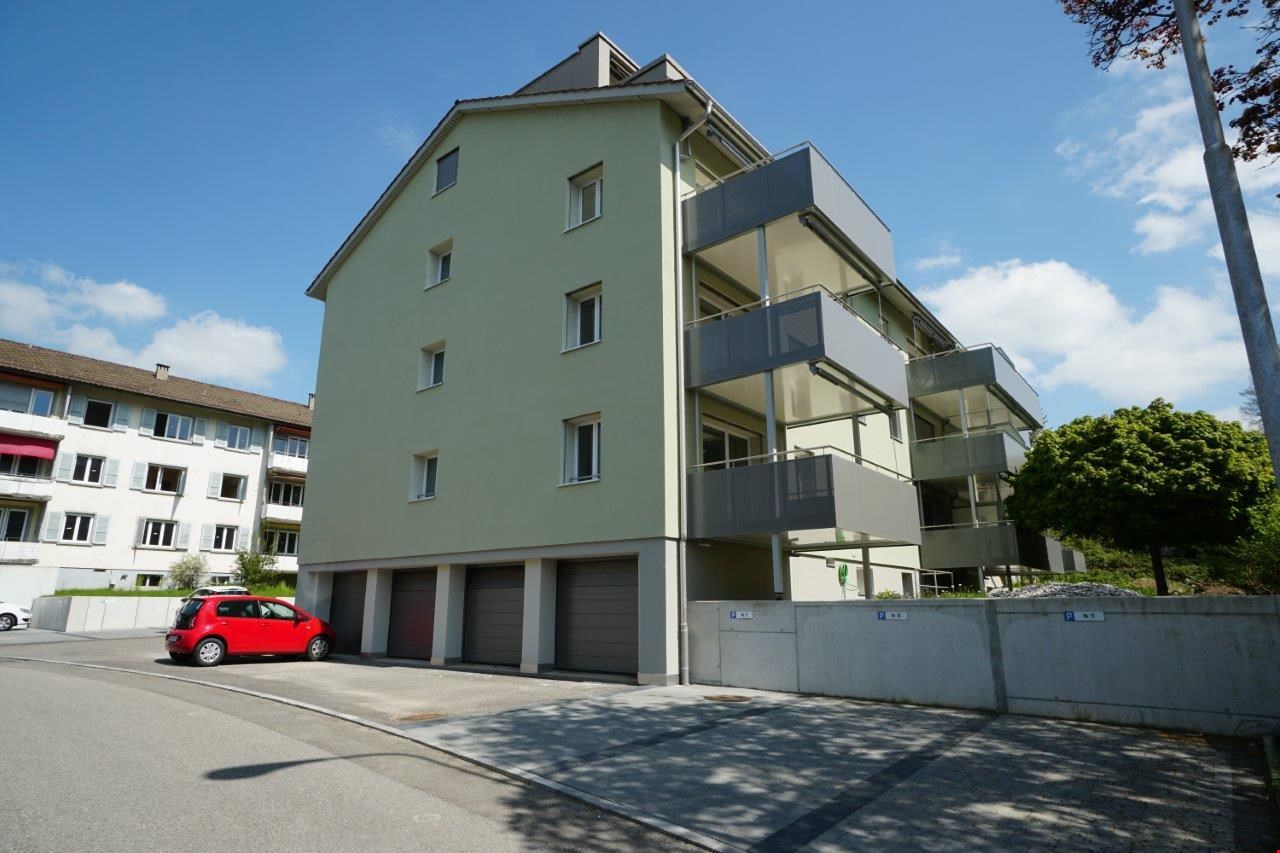4-story apartment building with green exterior, balconies, and parking spaces in the front