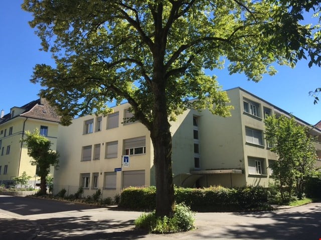 Apartment building, 5 stories, beige exterior, many windows, trees and bushes in front