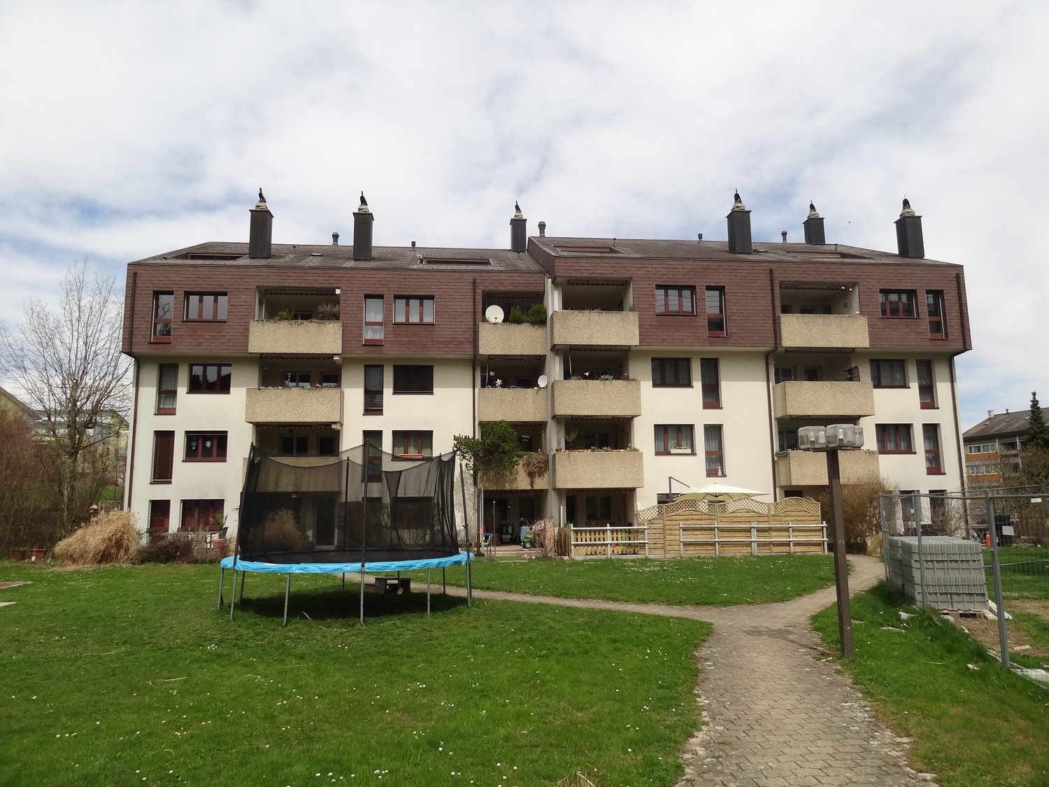 Apartment building with multiple floors, balconies, and a garden in front.