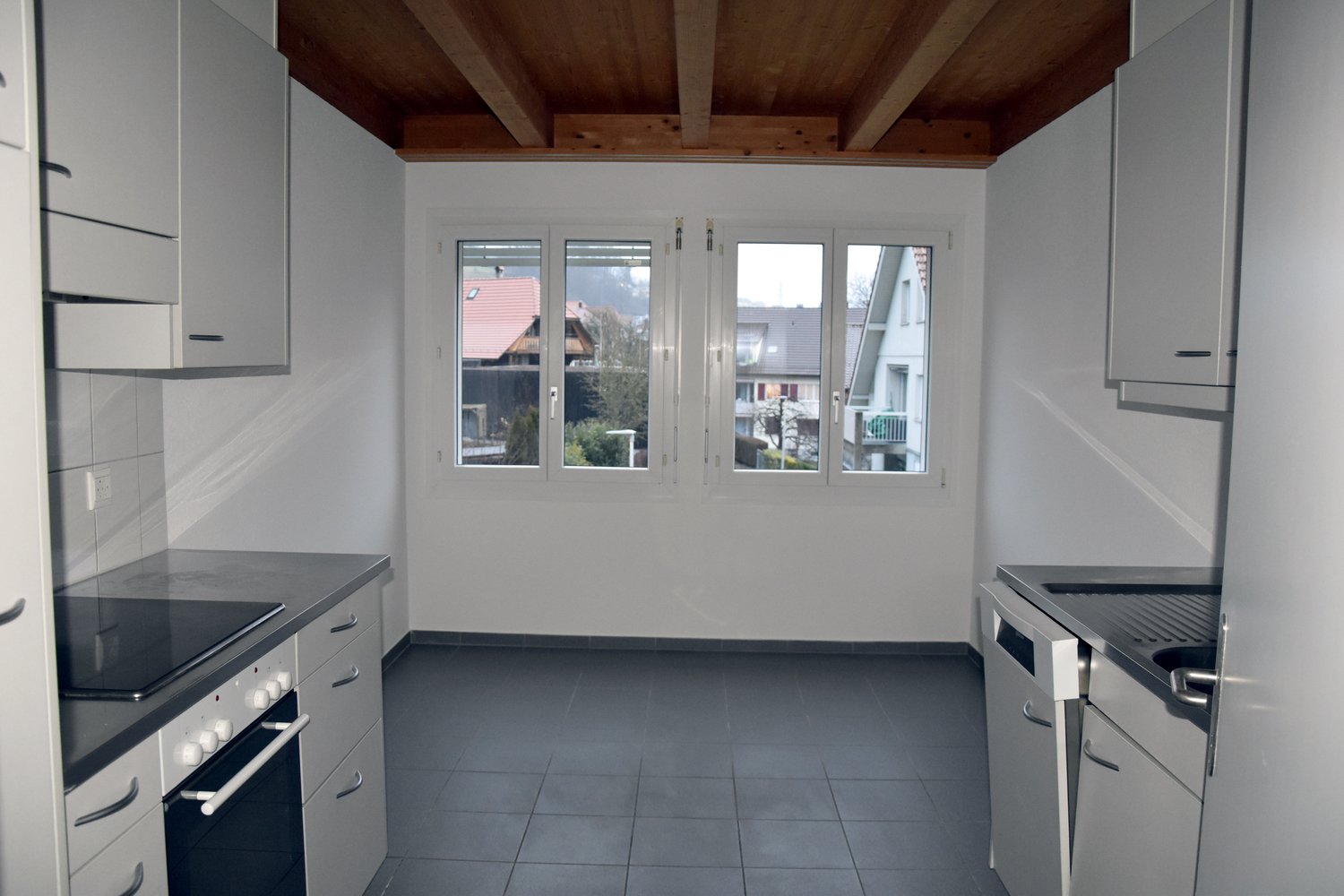 White kitchen, tiled floor, modern cabinets, black countertop, white appliances, large windows.