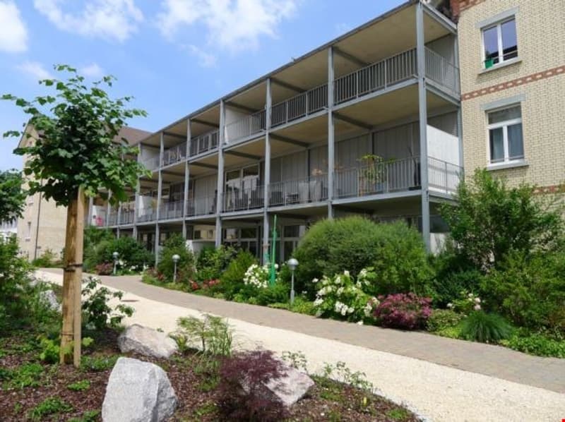 An apartment building with multiple balconies and a landscaped garden in front.