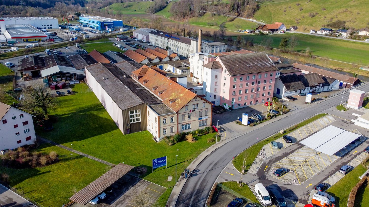 Industrial complex, various buildings, multiple vehicles, large open area, greenery, large parking area