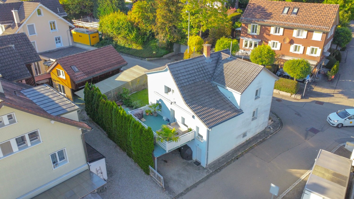 2 story house, tiled roof, driveway, balcony, plants, trees, nearby buildings