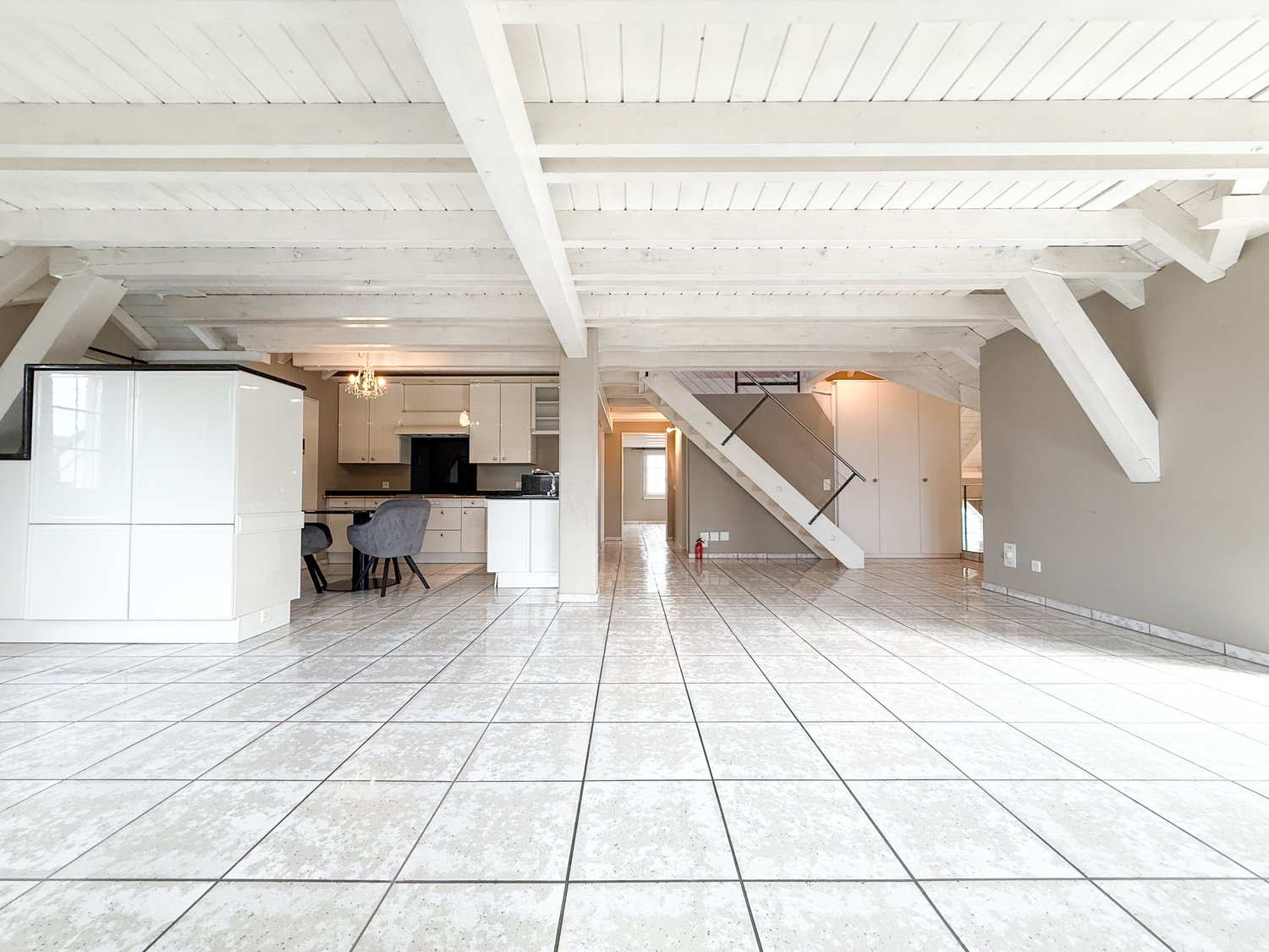 Open space room, tiled floor, white walls, white kitchen, staircase, dining table, chairs