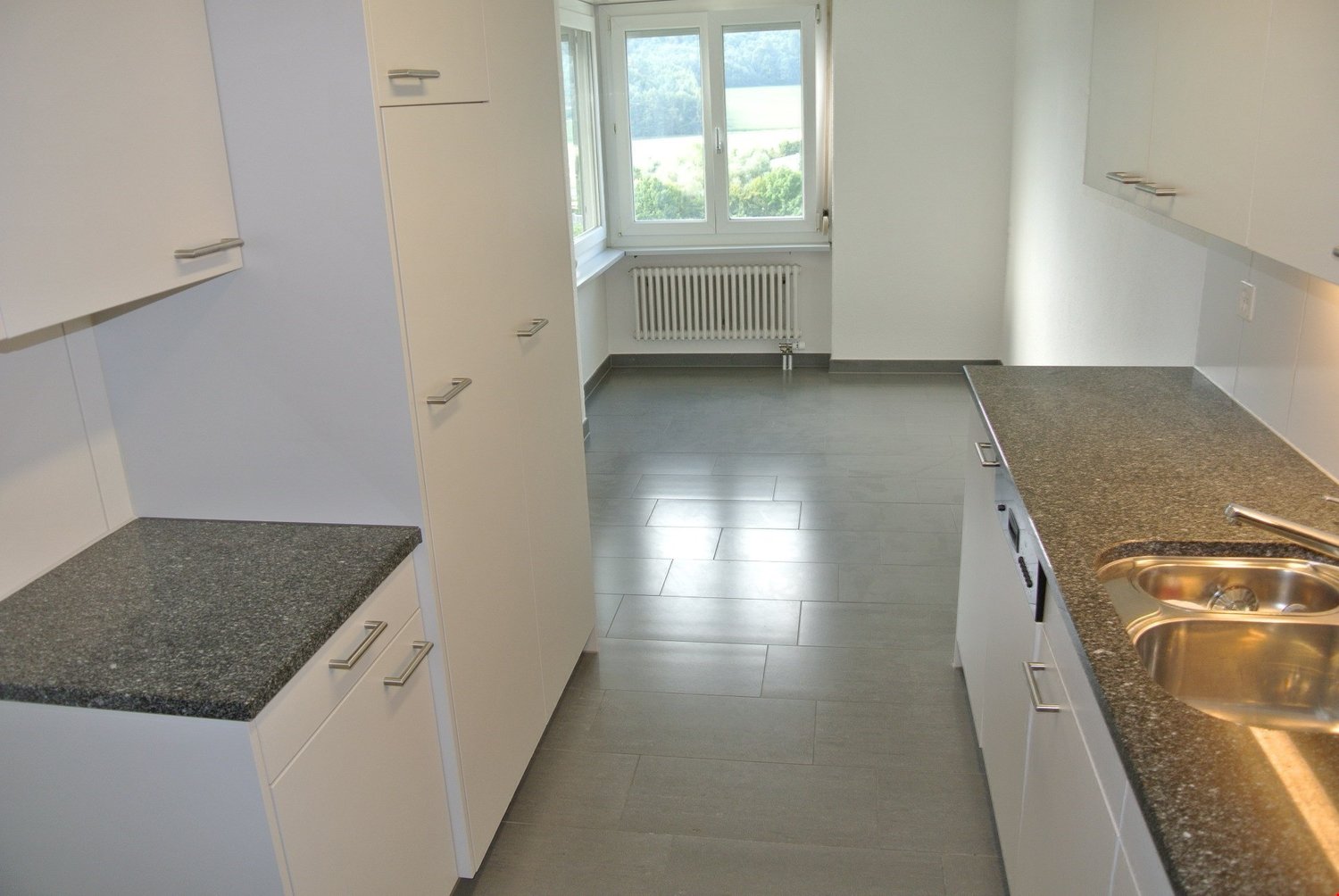 Minimalistic kitchen with granite countertops, stainless steel sink, white cabinets, tiled floor, and windows with valley view