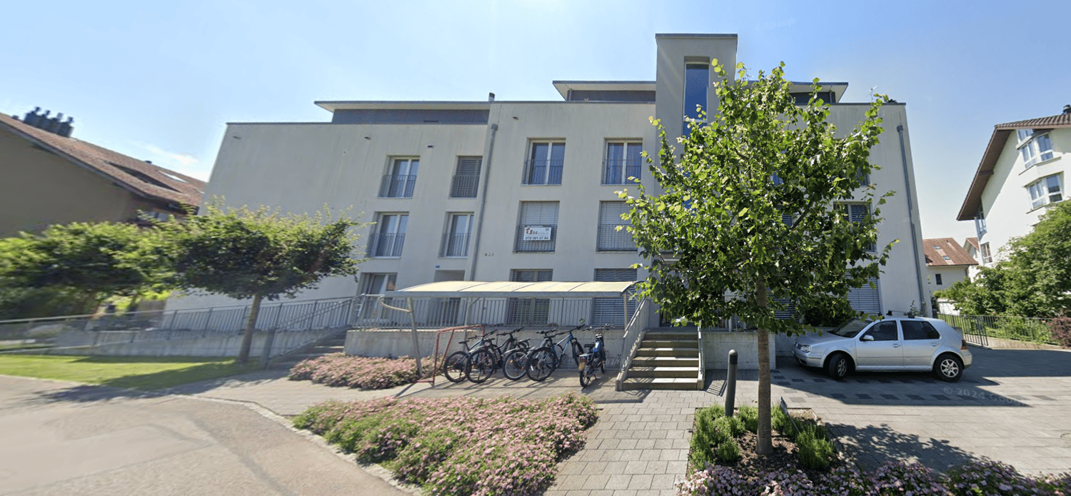 White building with 3 floors, 6 bicycles parked, one car parked, stairs, garden in front.