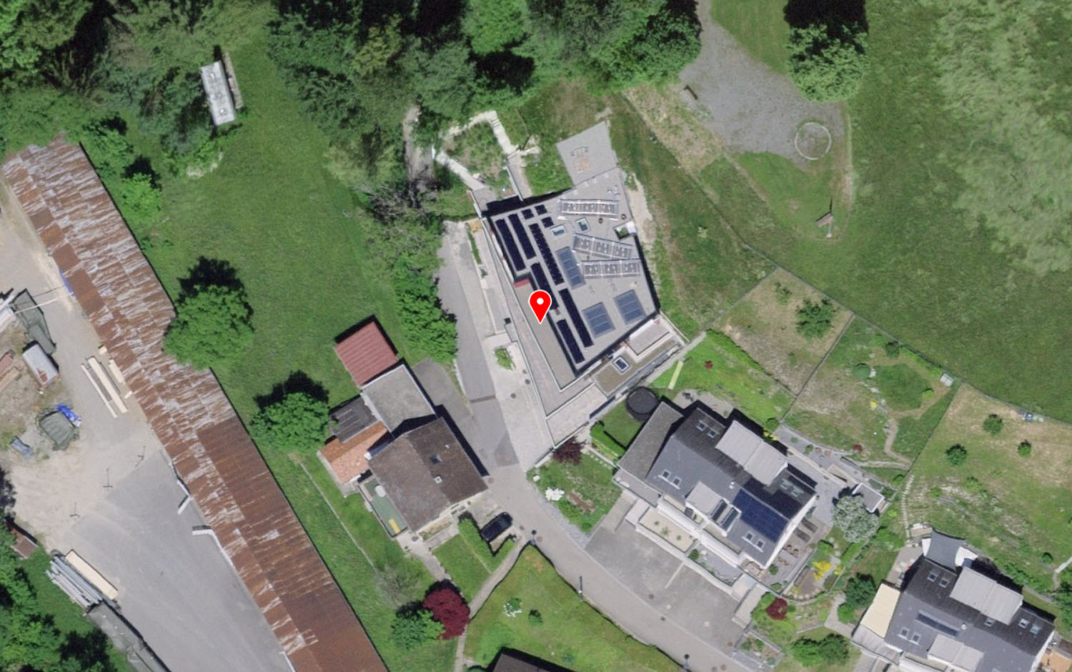 Aerial view of a small housing complex with a garage, multiple residential buildings, a parking area, and green surroundings.