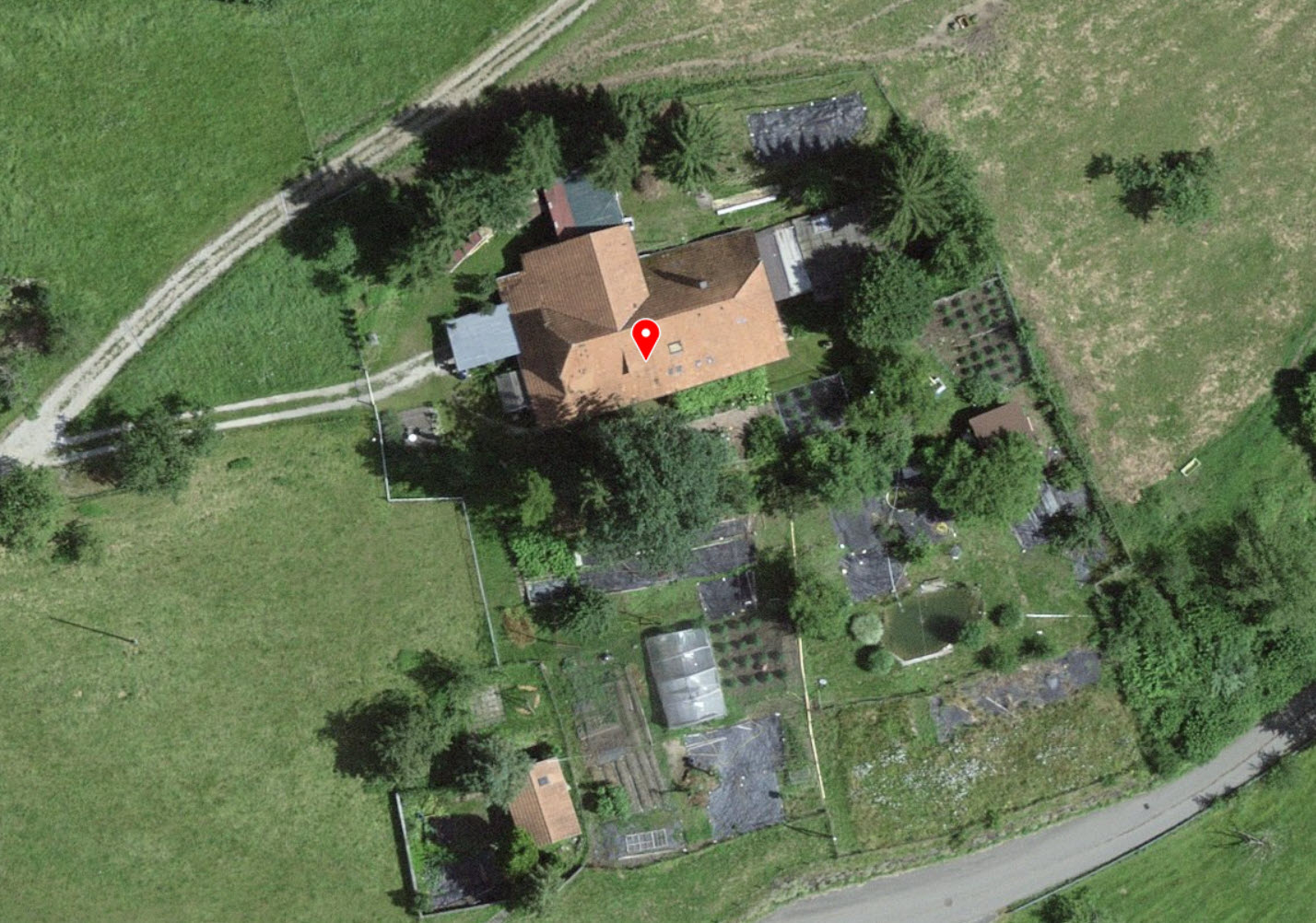 House with surrounding garden, several greenhouses, located on rural landscape.