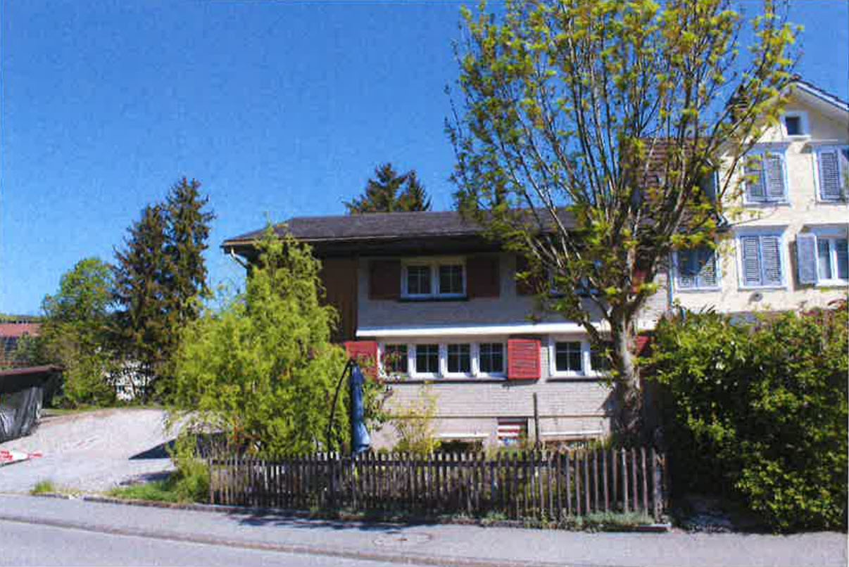 Two story house, gray roof, red shutters, driveway, fenced yard, trees, mountain view