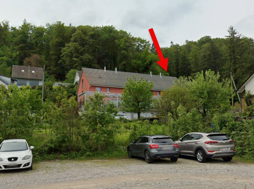 a two story house with red brick facade and gray roof with two garage doors at the bottom and a car parked nearby