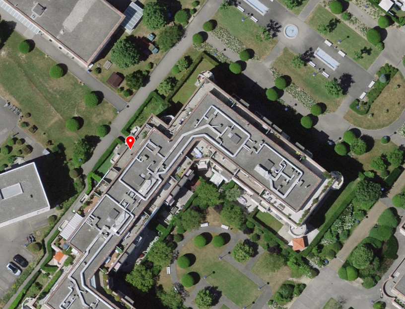 Aerial view of a building complex with multiple buildings, surrounded by trees and grass, and a parking lot.