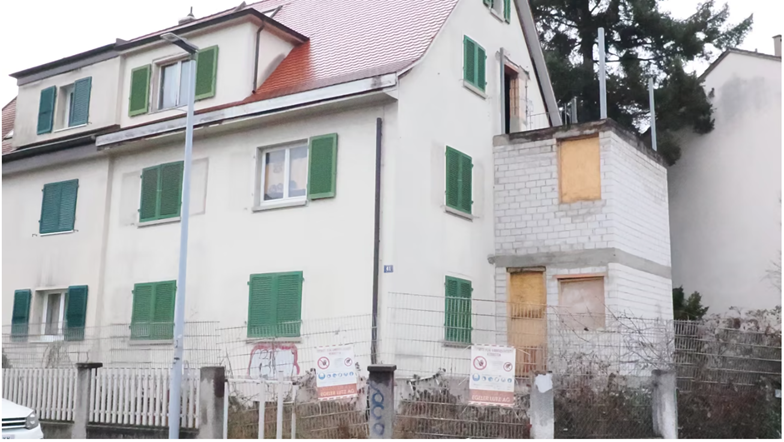 3 story house, white exterior, green shutters, red roof, fenced yard, some windows boarded up