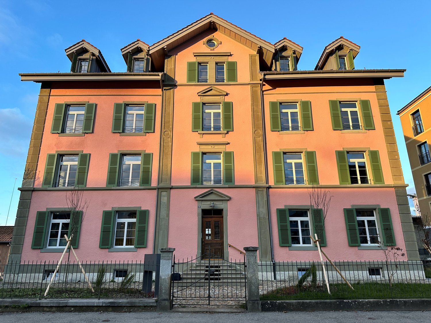 4 story building, pink walls, green shutters, arched doorway, black gate, front garden, stairs