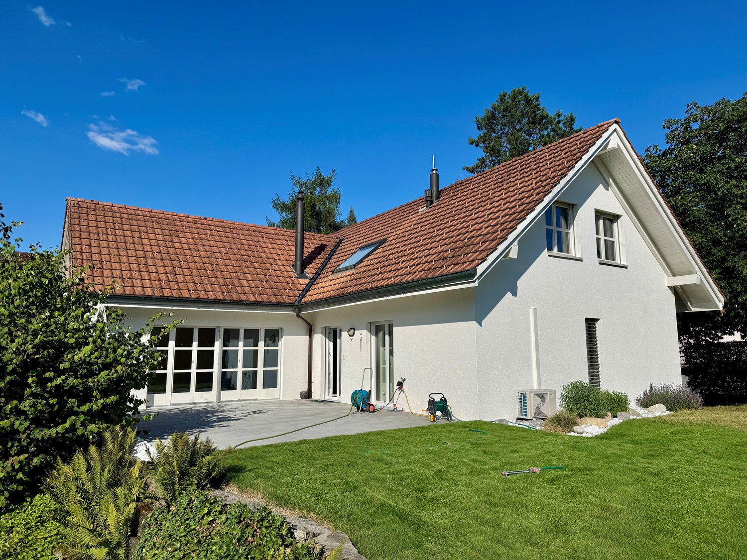 modern house, red roof, white walls, large windows, garage, landscaped lawn, trees in the background