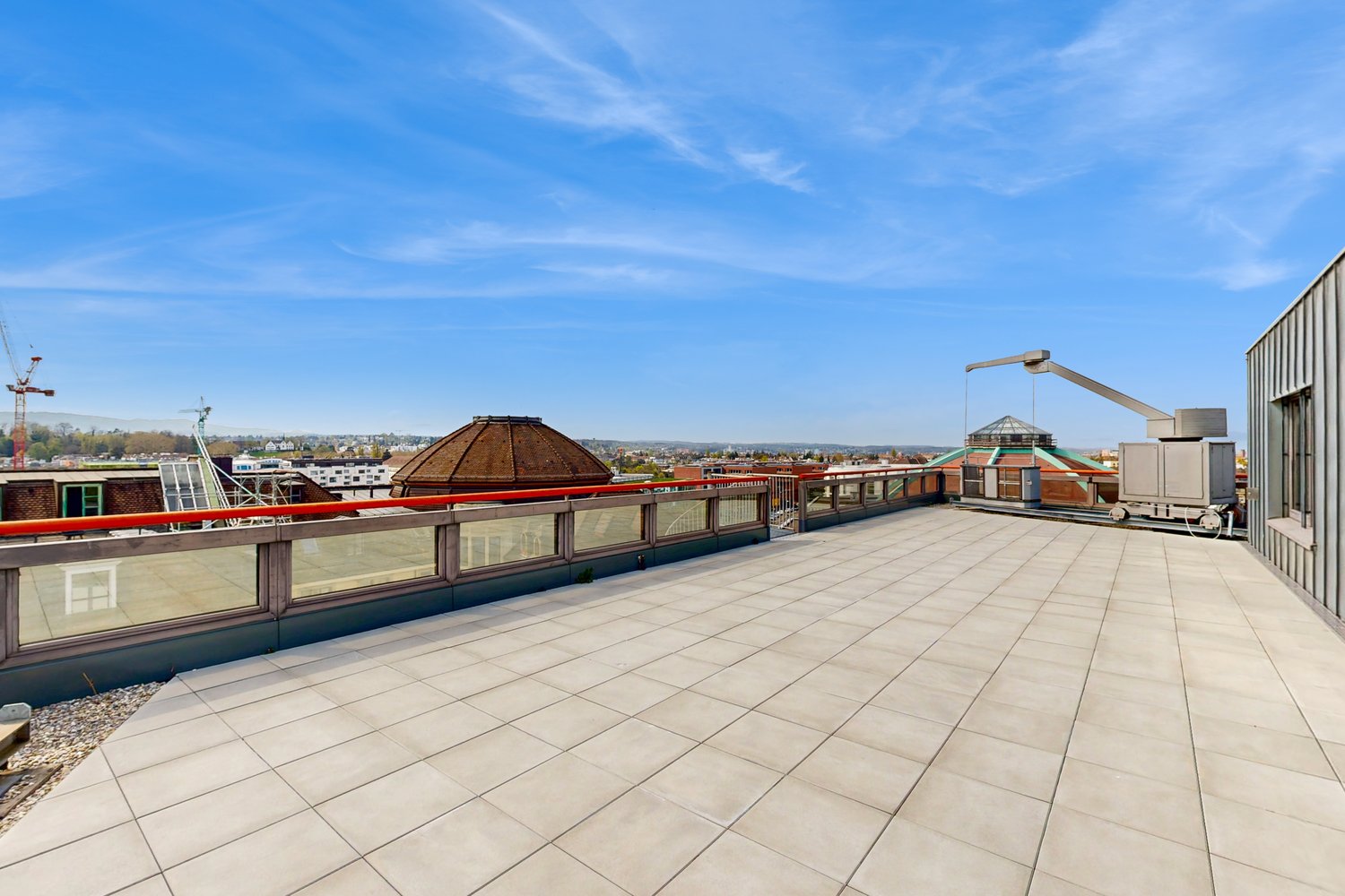 Large open rooftop terrace with tiled flooring, glass railings, and views of the surrounding cityscape. The terrace features a domed structure and other architectural elements.