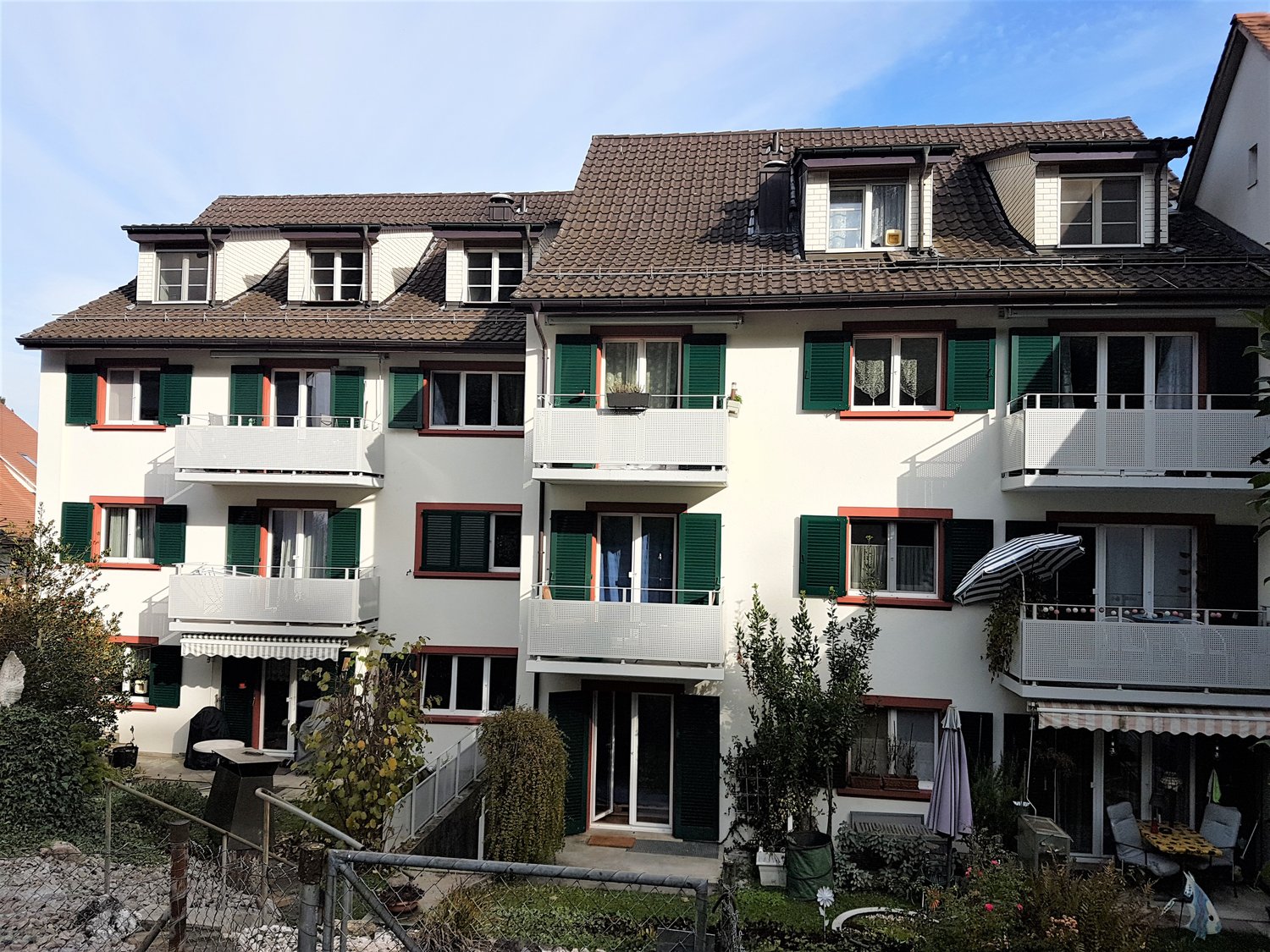 3 story apartment building, white walls, brown roof, green shutters, balconies