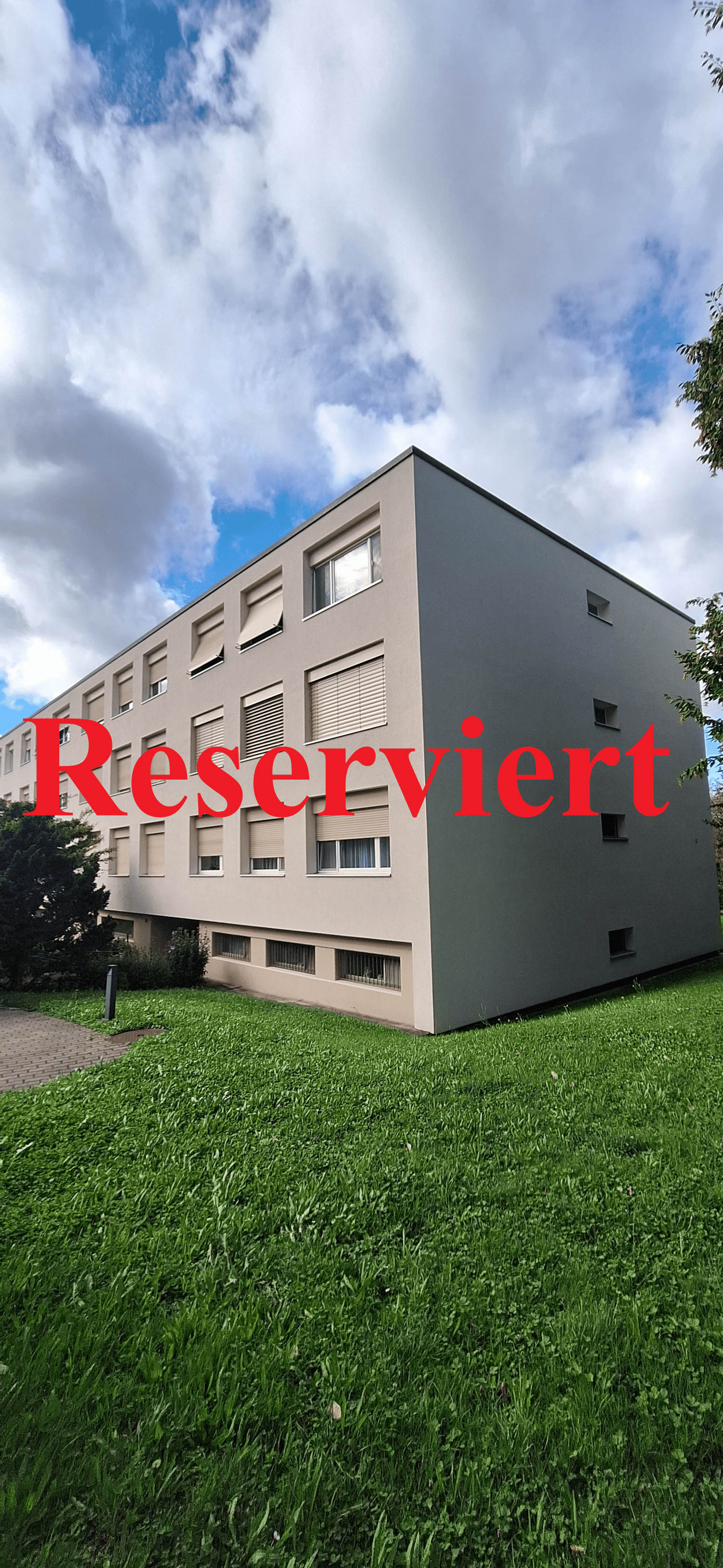 A three story building with windows, grass, cloudy sky