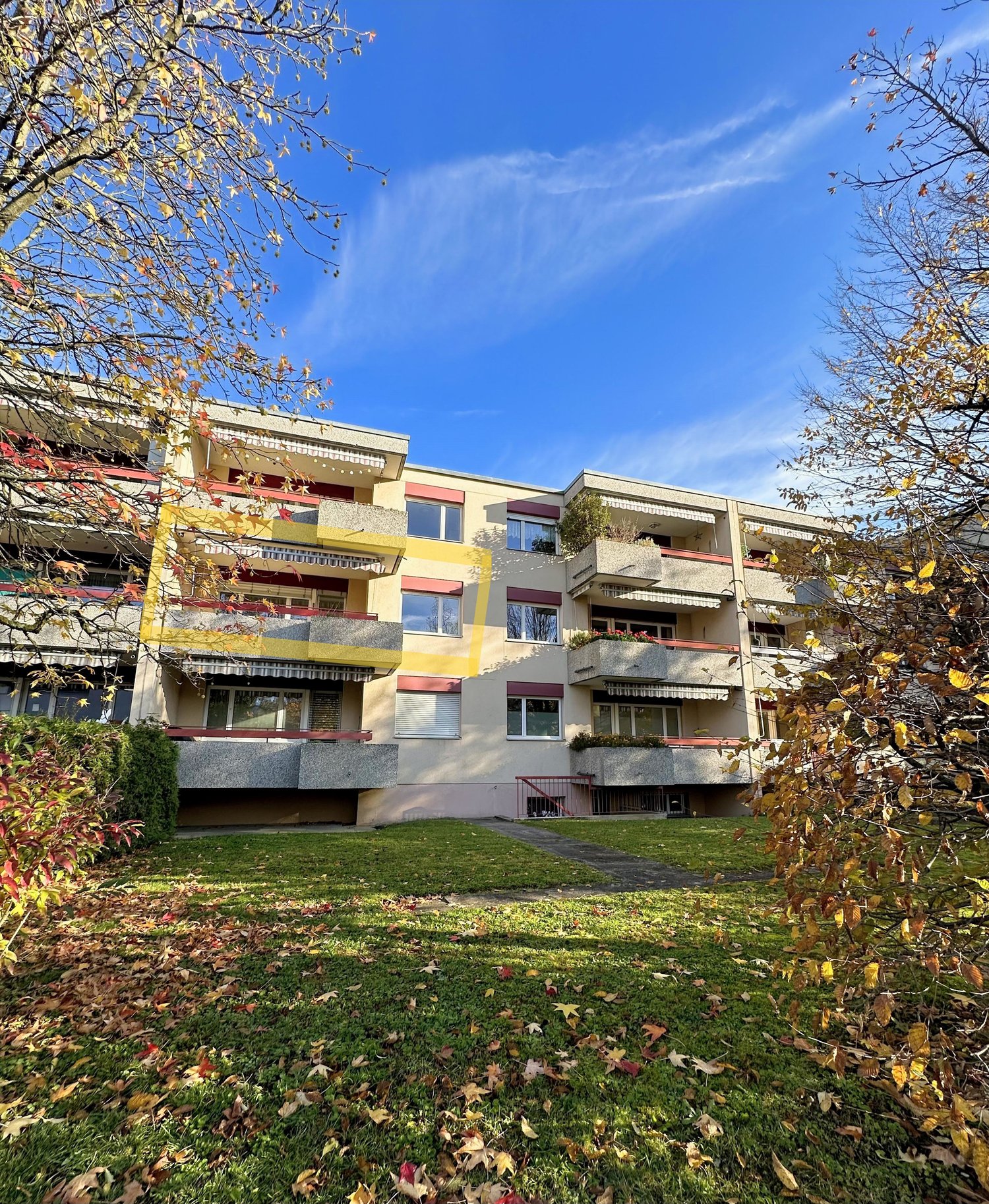 3-story apartment building, beige walls, yellow accents, balconies, multiple windows, fenced yard