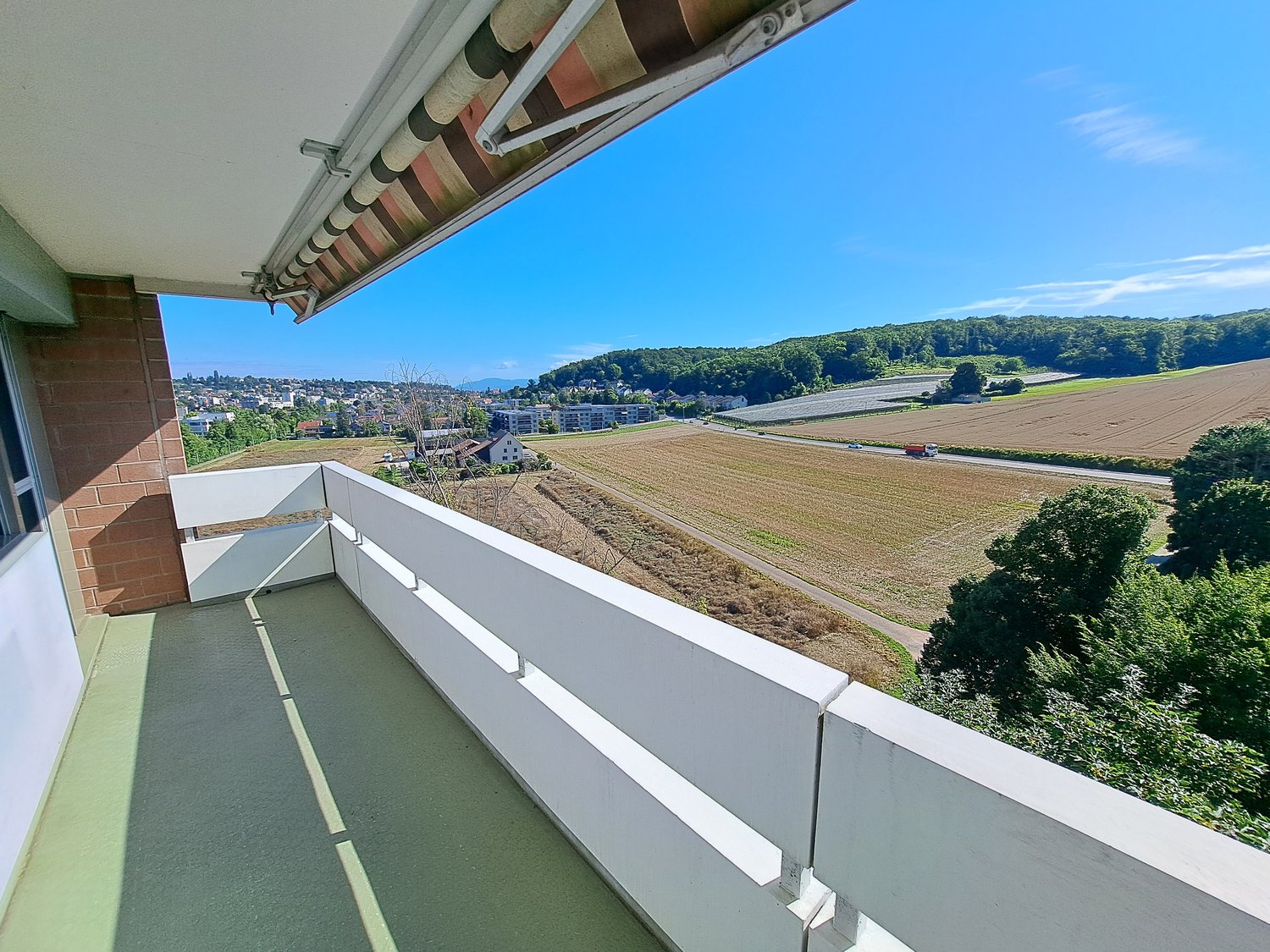 Balcony with a view of a vast field and a road with moving vehicles