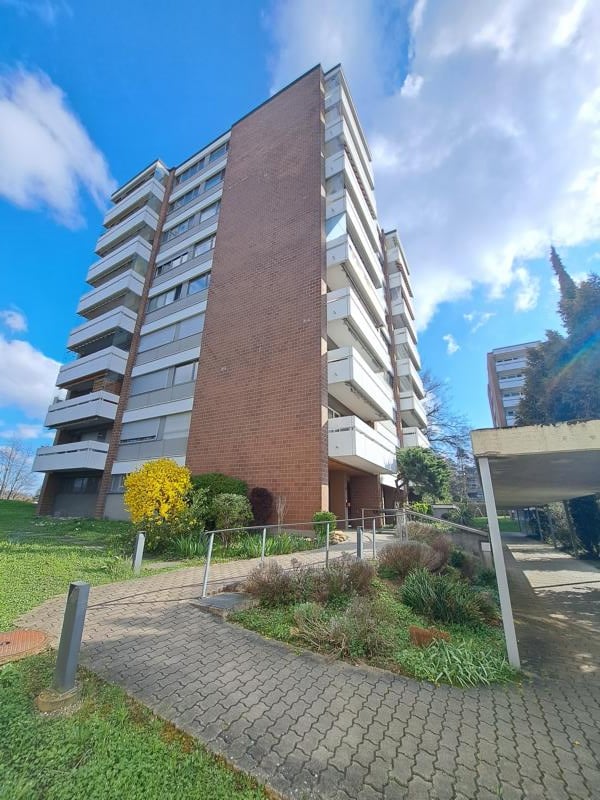 modern brick high-rise building, many windows, balconies, paved path leading to the entrance, greenery