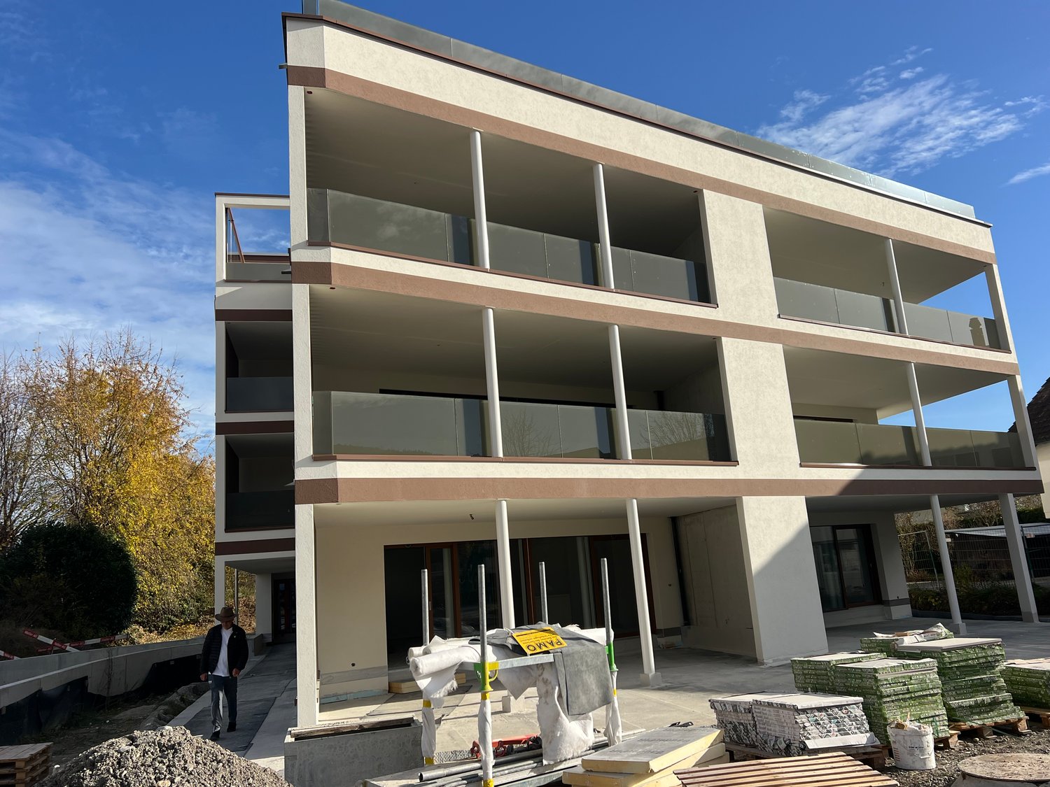 Modern multi-story building, glass railings on balconies, white walls, gray accents, under construction