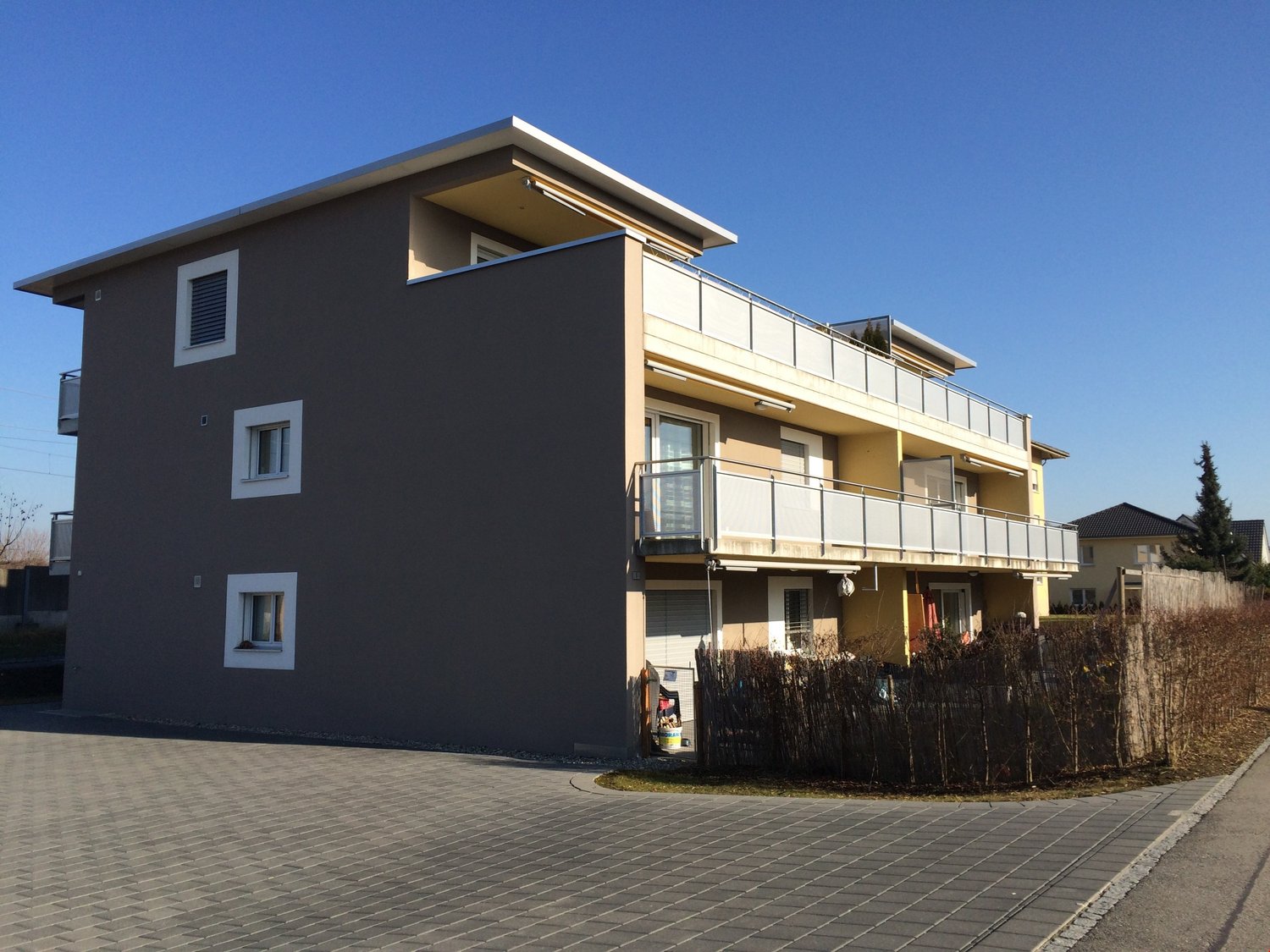 2-story house, grey exterior, white windows, balconies, paved parking area