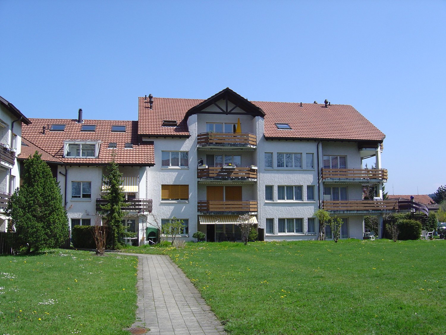 3 story apartment building, white paint, red tile roof, balconies on each floor, large front yard