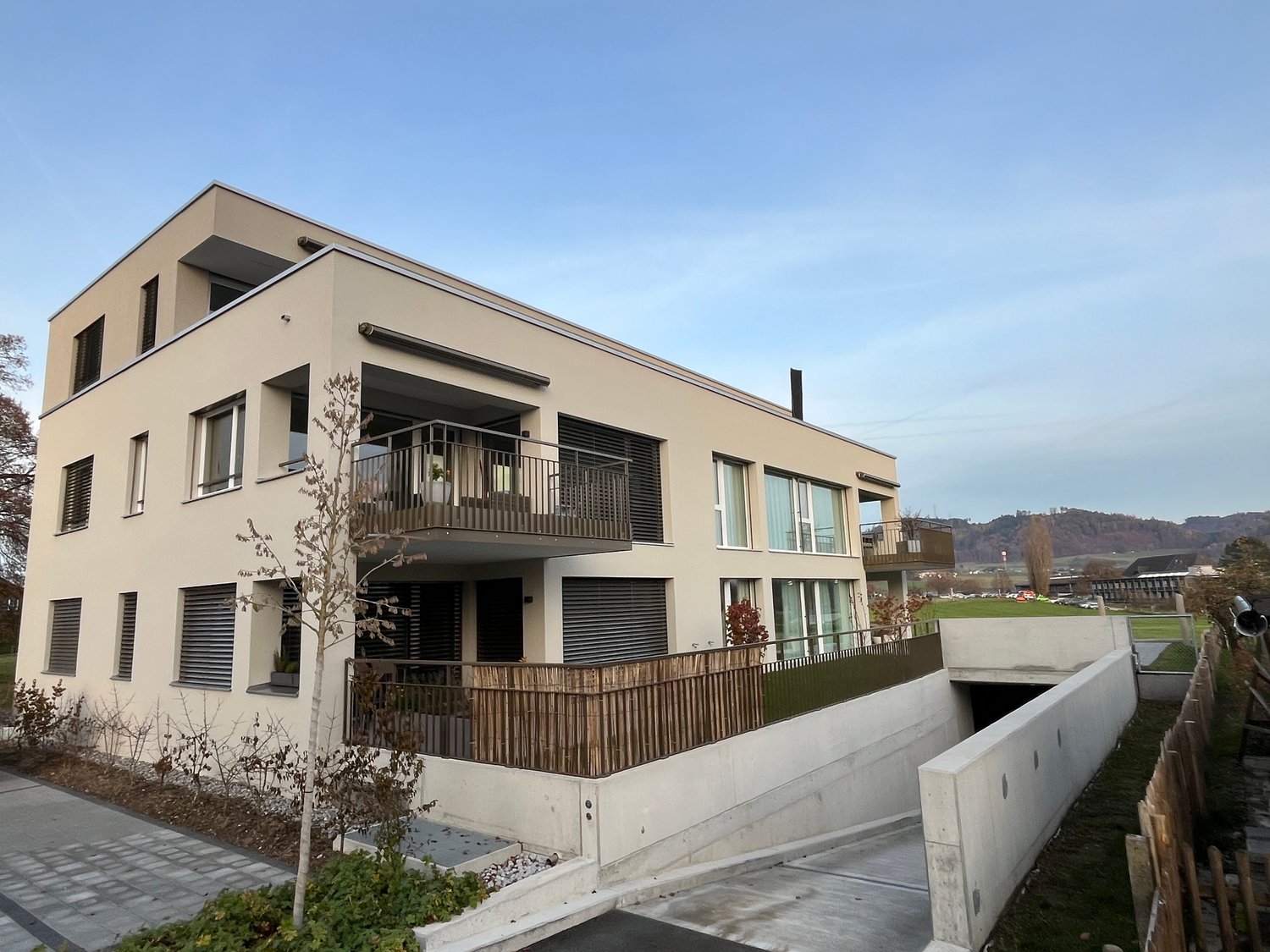 2-story apartment building, balcony on the upper floor, white walls, metal railings, large windows, concrete pathway in front, metal barriers on the sides.