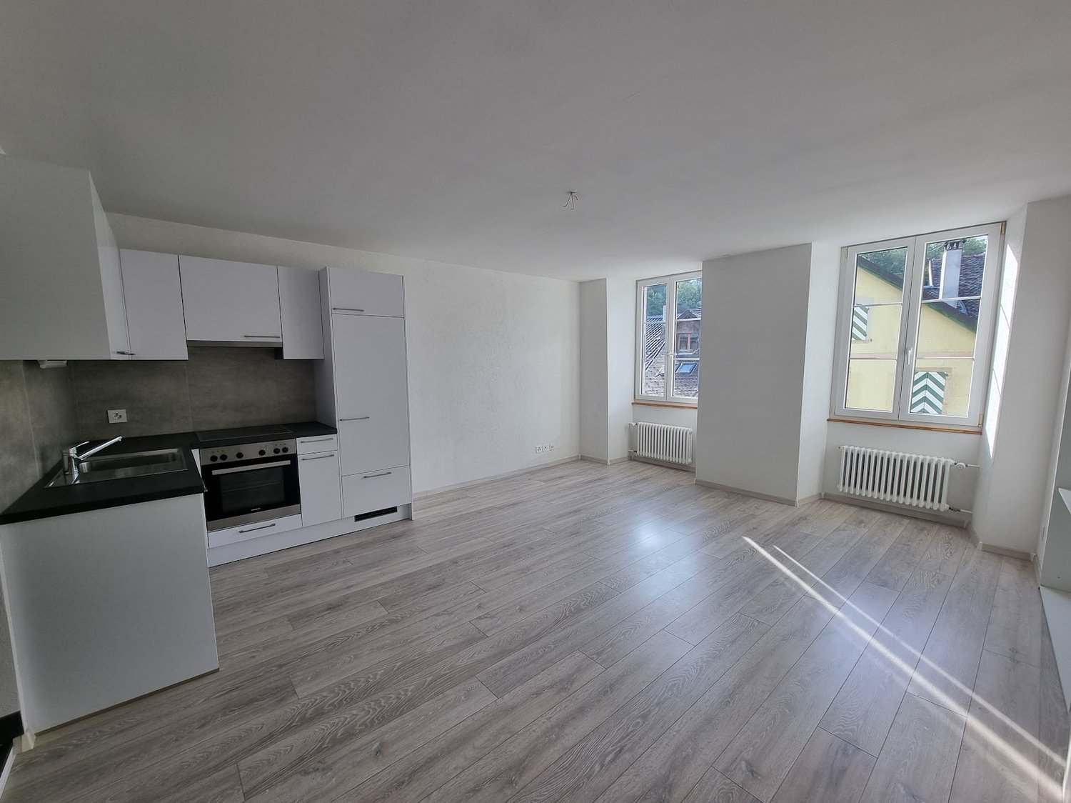empty kitchen with white cupboards, black countertop, modern appliances, windows with a view